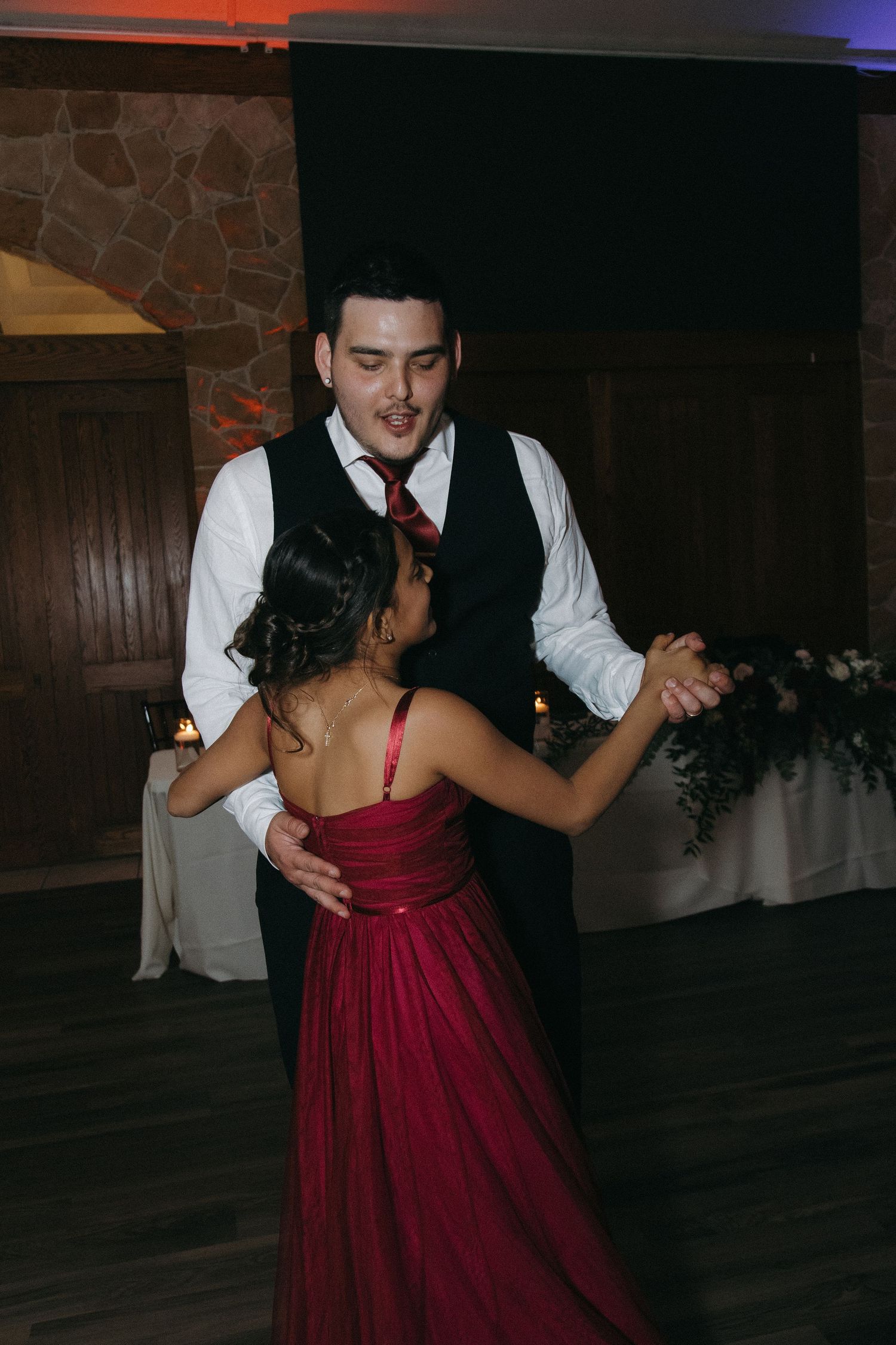 Groom dancing with bridesmaid in red gown at elegant wedding reception celebration.