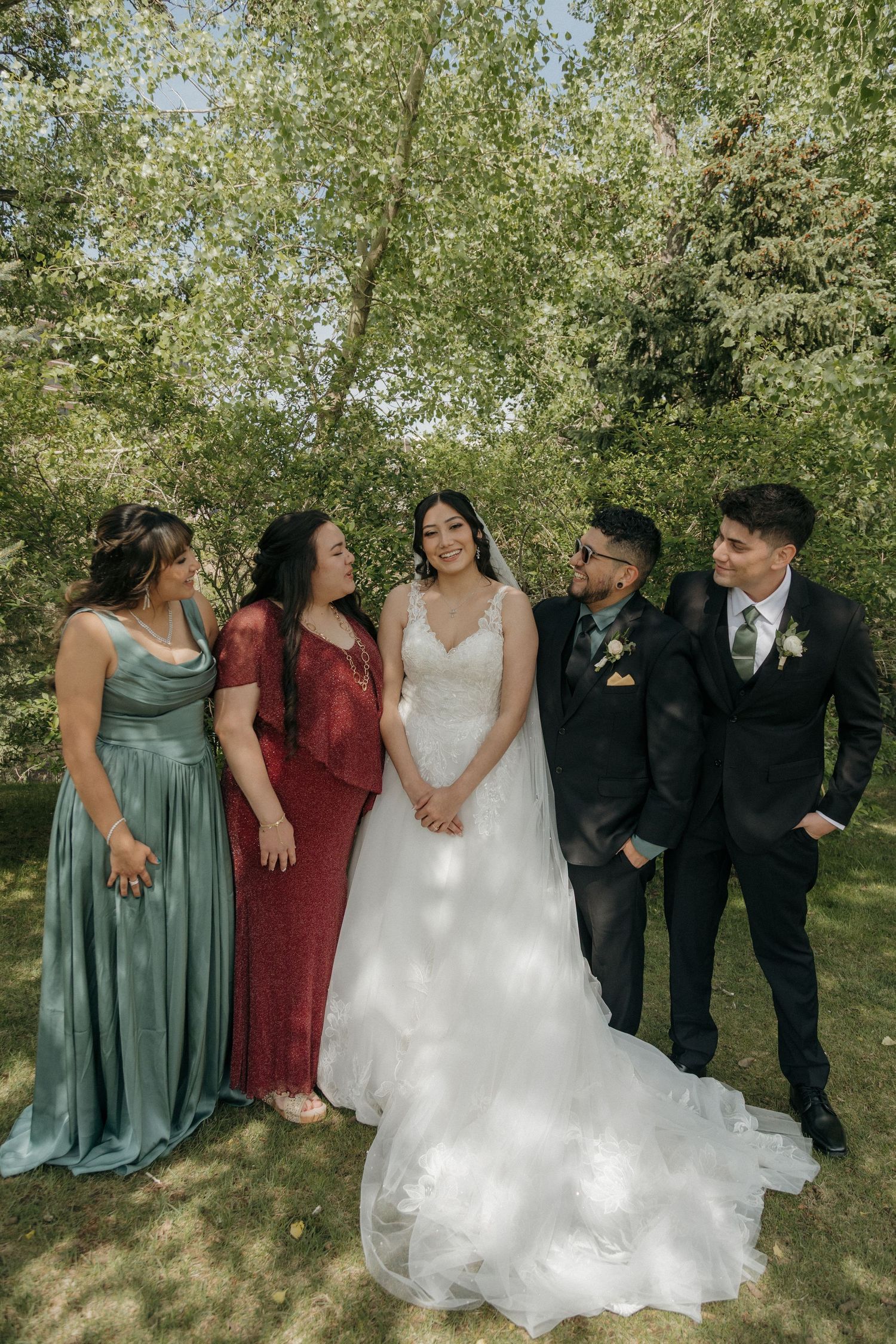 Bride poses with bridesmaids and groomsmen under a beautiful tree on her wedding day.