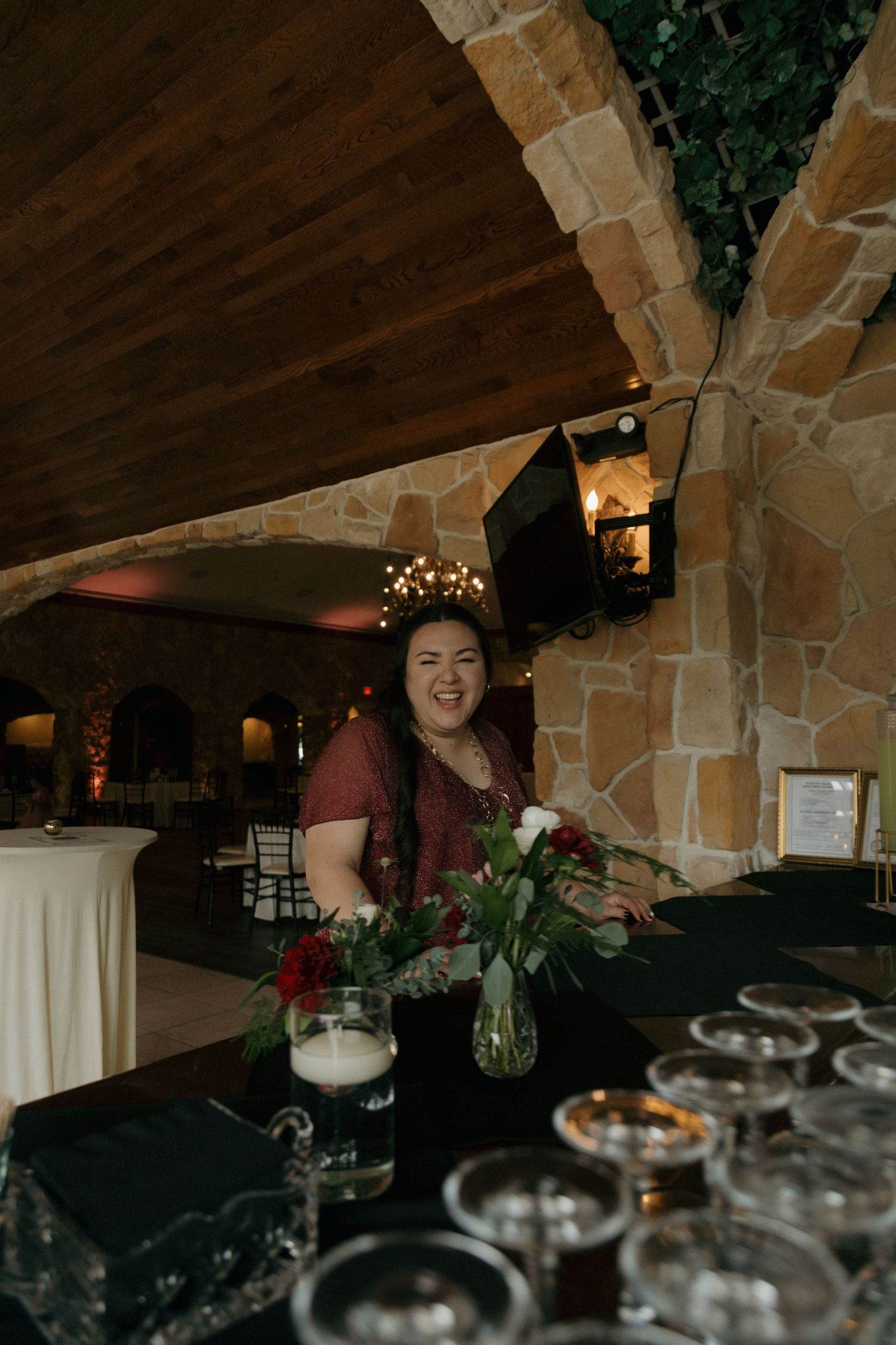 Smiling woman standing behind a bar decorated with red and white floral arrangements.