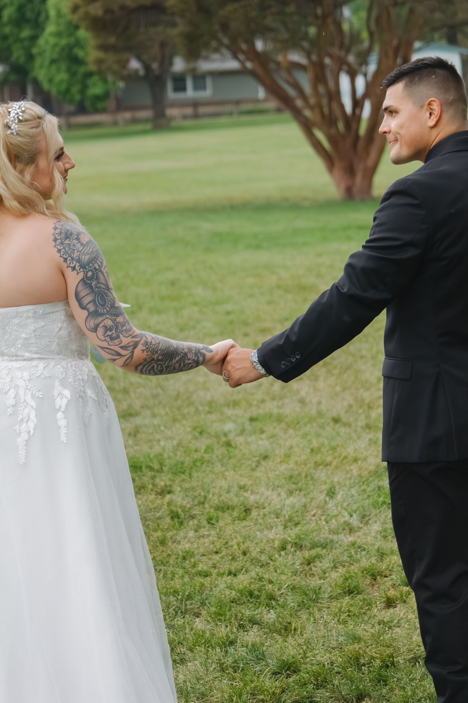 Couple holds hands while wearing formal wedding attire outdoors.