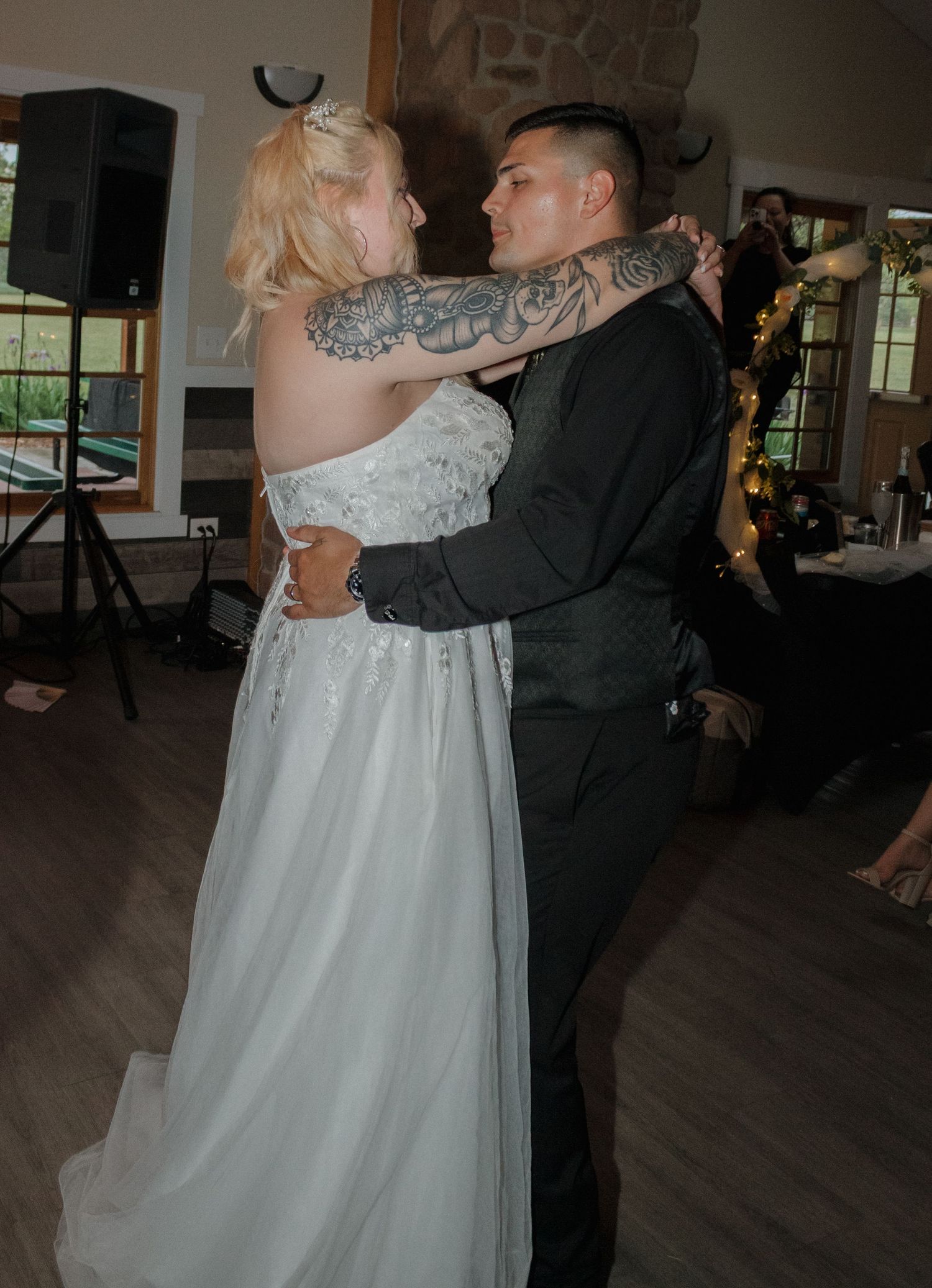 Dancing couple embraces on a hardwood dance floor during what appears to be a wedding reception.