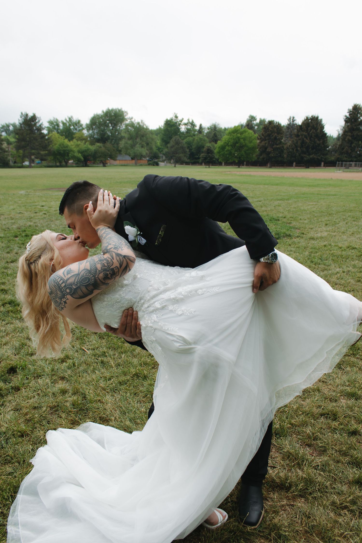 A dramatic dip pose between newlyweds on their wedding day in a grassy field.