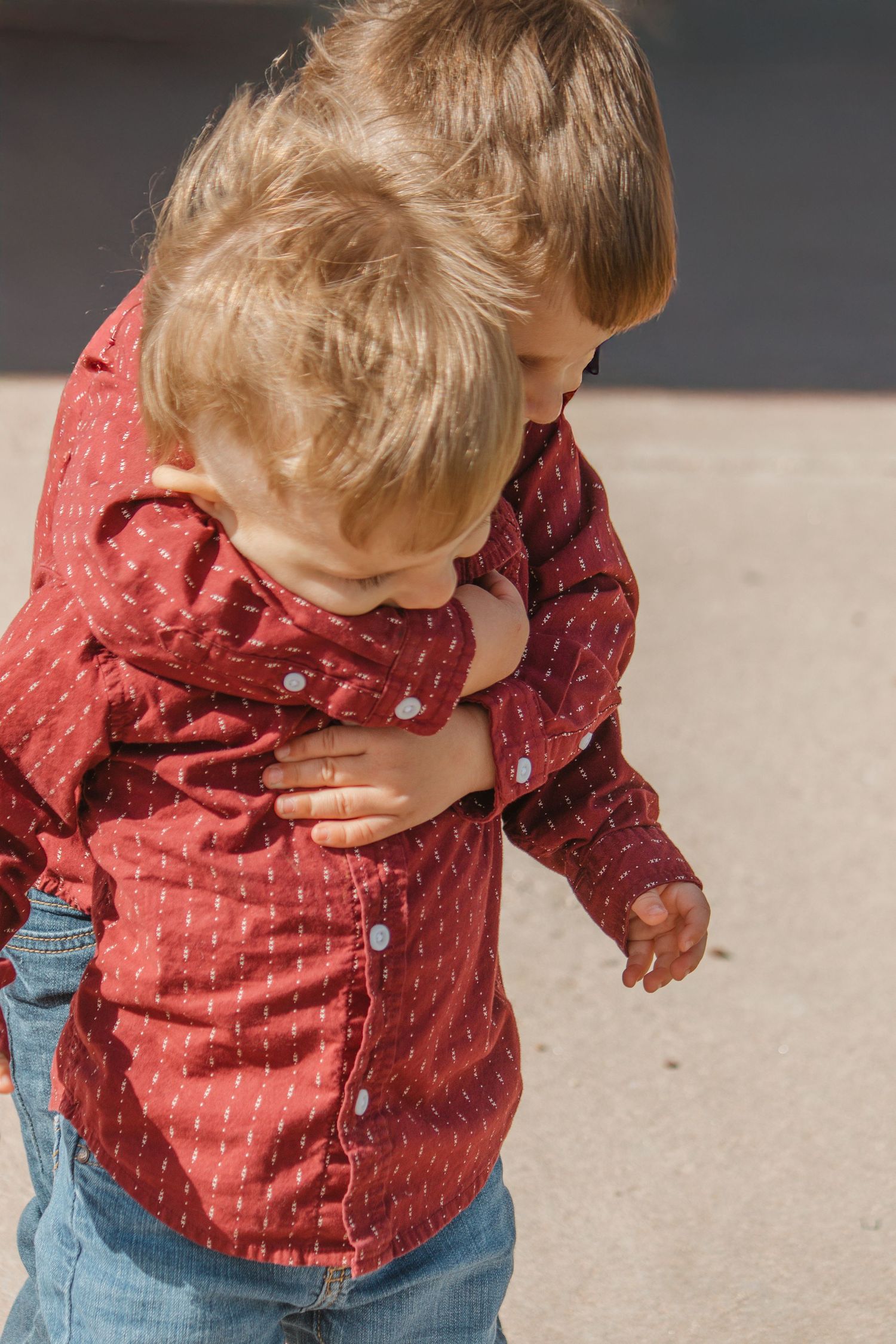 Young child in a red patterned shirt and jeans plays outdoors.