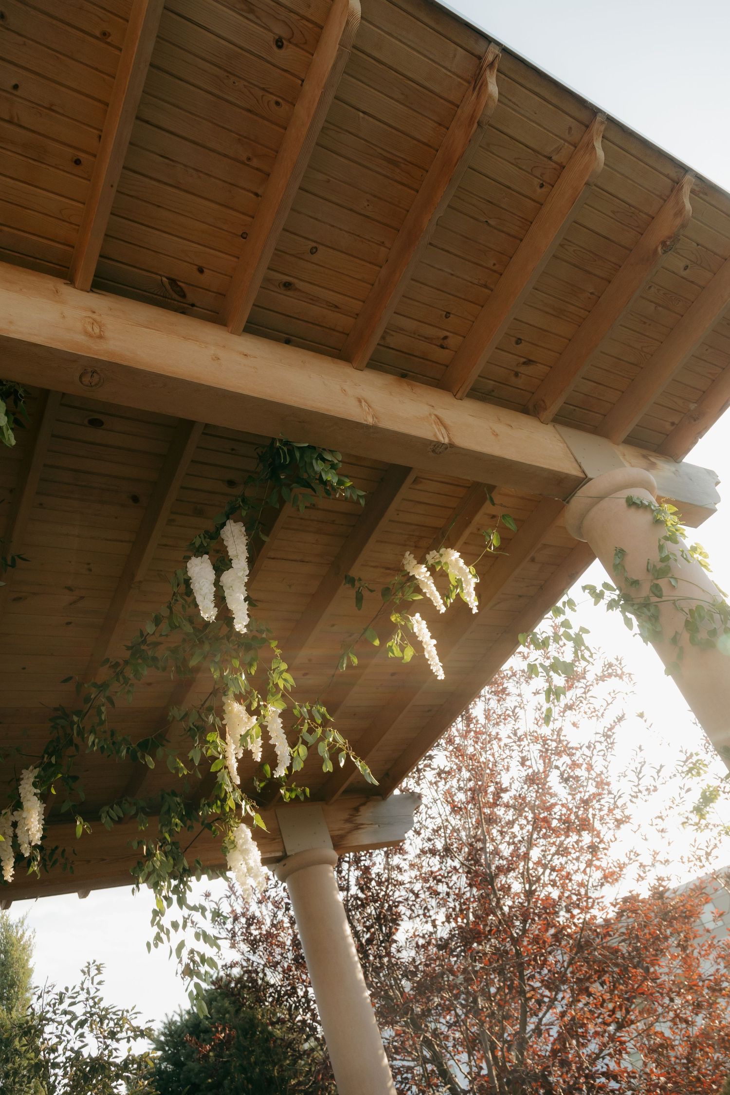 Wooden pergola adorned with cascading white flowers and greenery at an outdoor wedding venue.