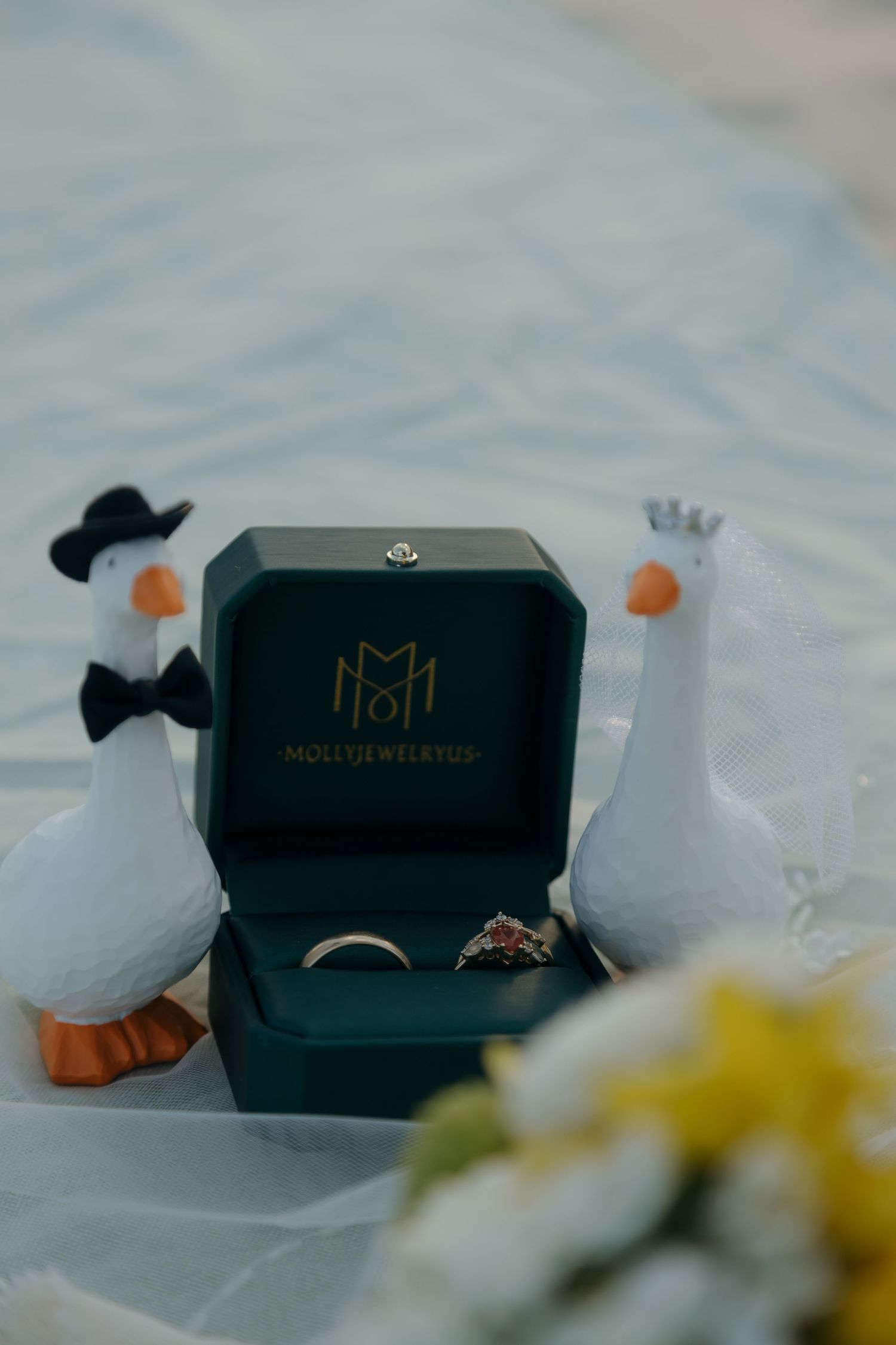 Wedding rings in green velvet Molli Jewelers box flanked by ceramic duck figurines.