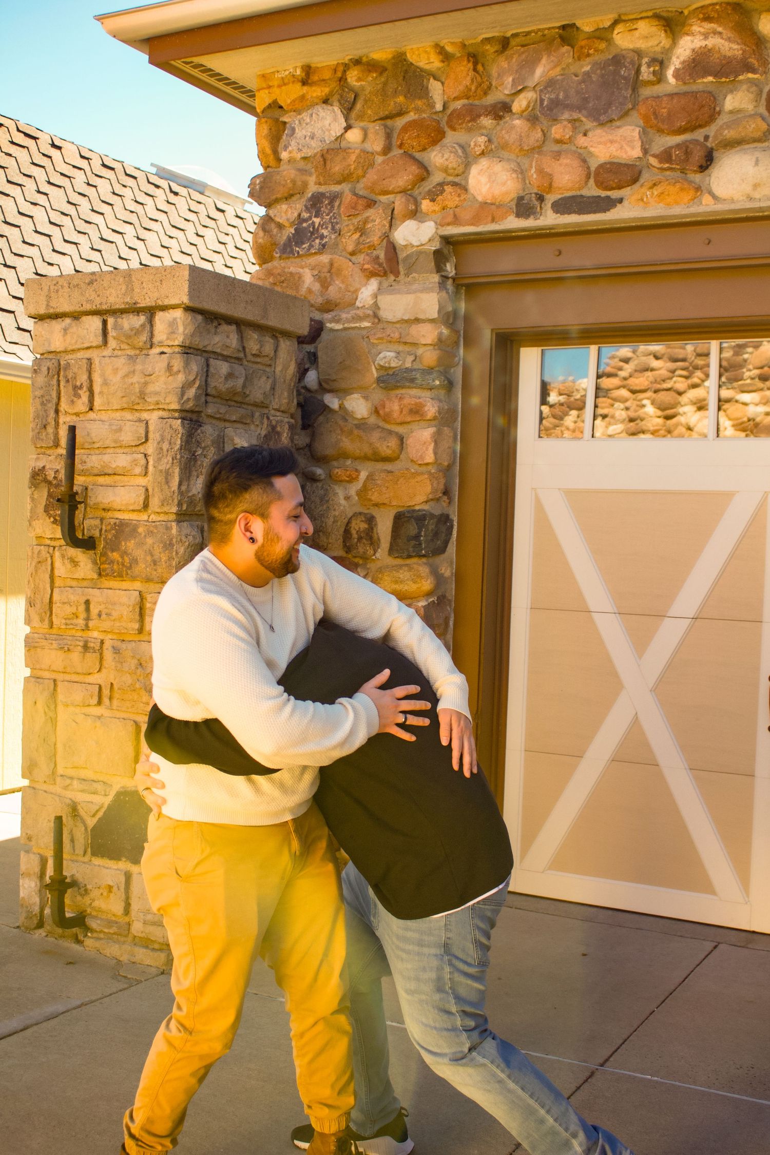 Two people playfully embracing near a stone and brick garage entrance.