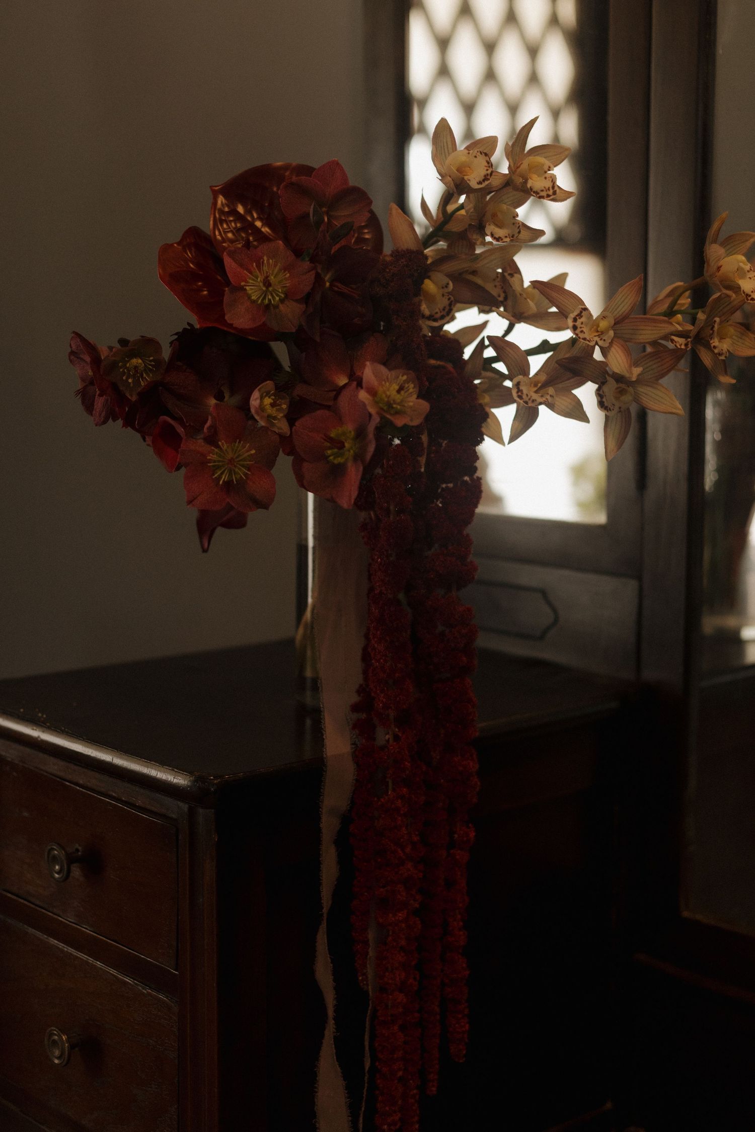 Dried autumn flowers in a vase cast dramatic shadows against a white wall near a window.