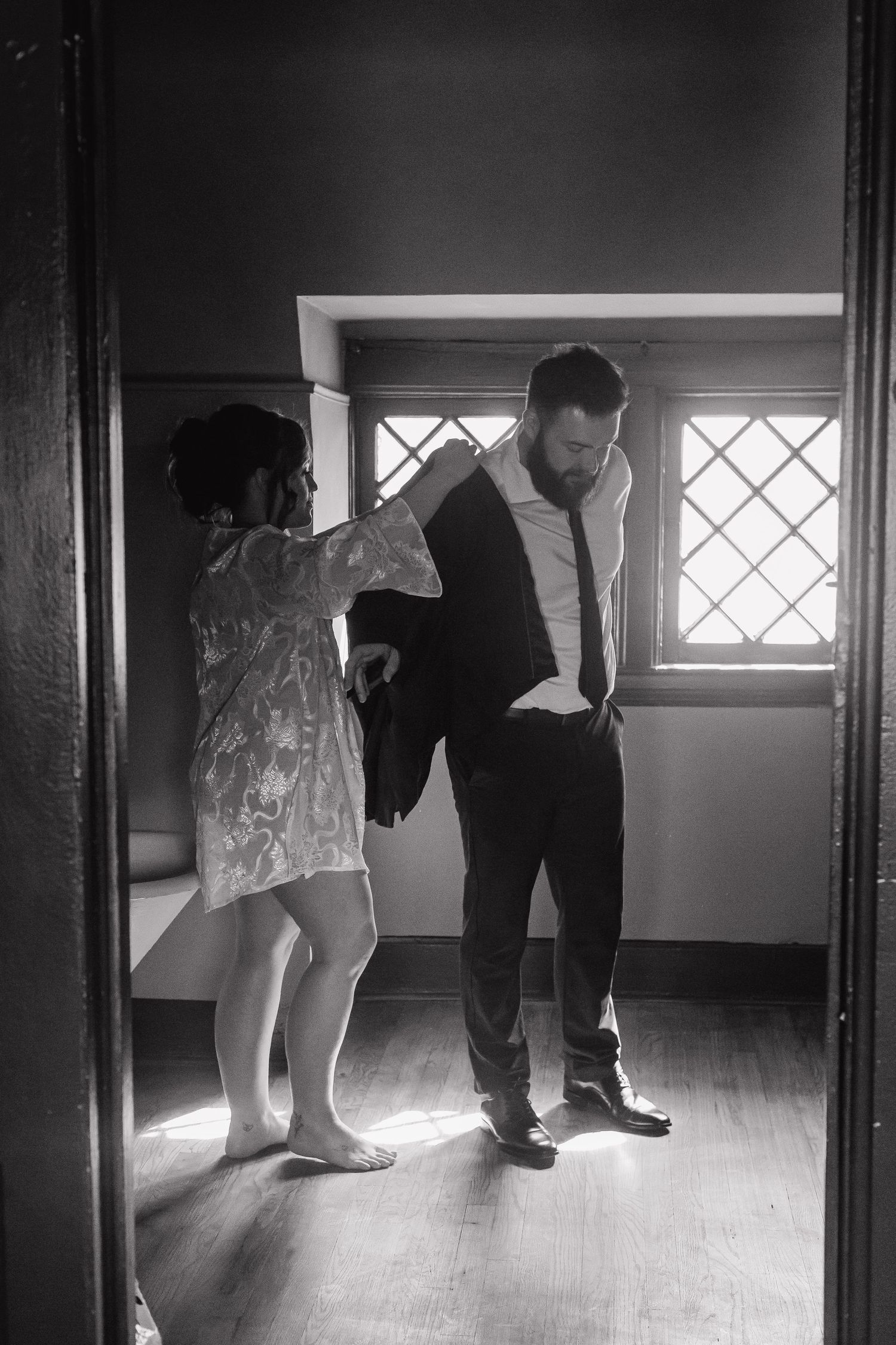 A black and white photo showing wedding day preparations in a sunlit room with diamond windows.