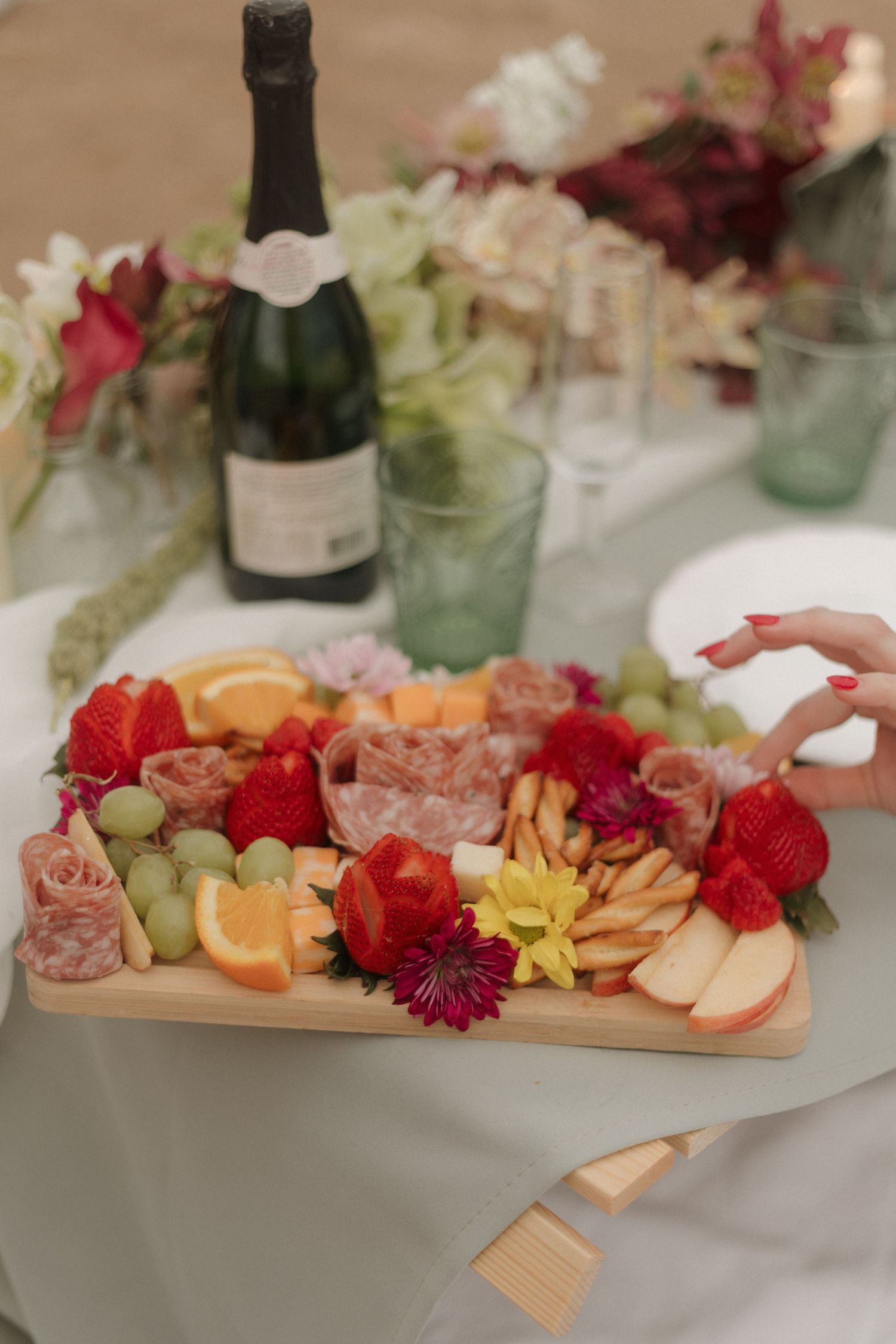 Elegant charcuterie board with fresh fruit, flowers and champagne at wedding reception.
