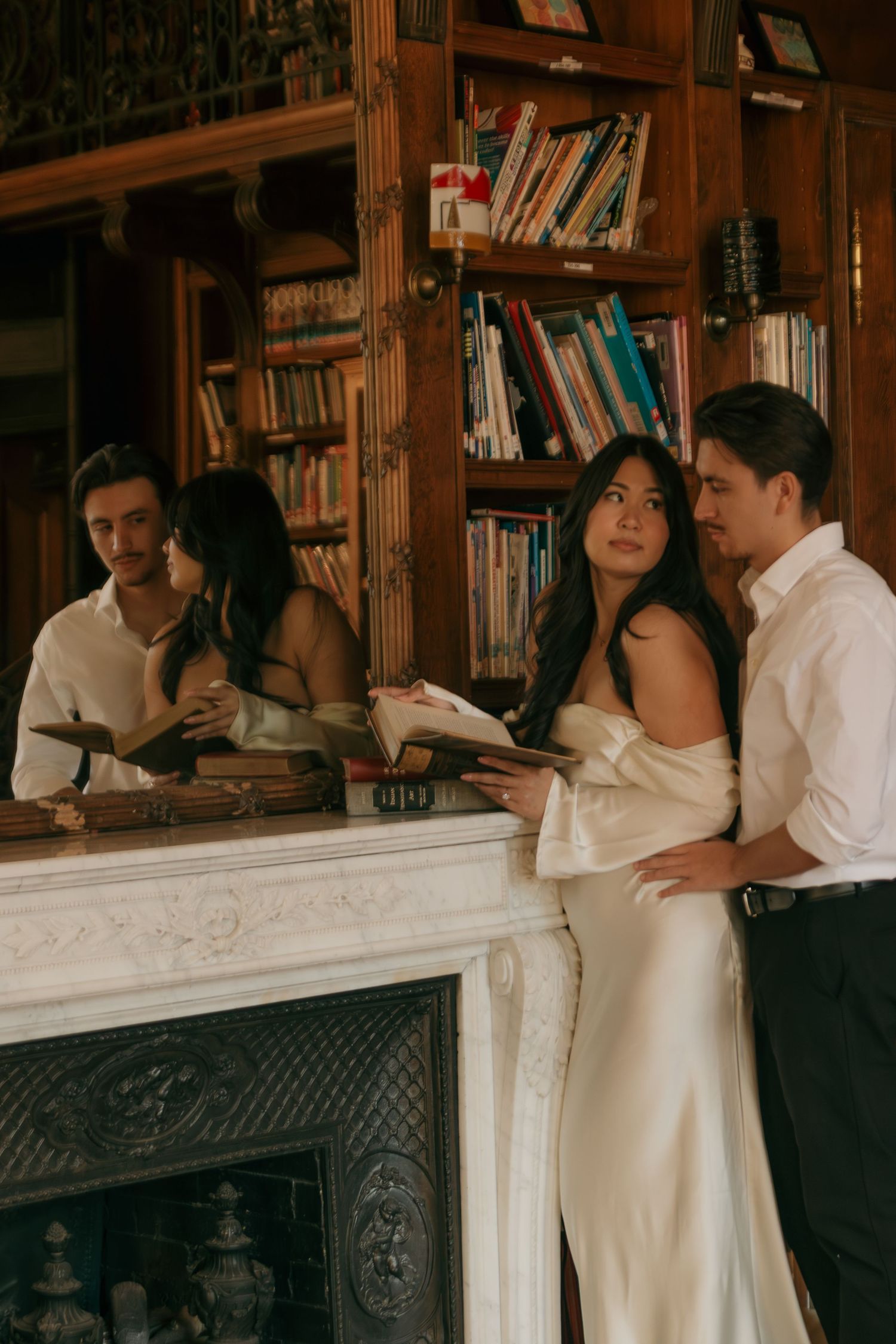 Romantic couple photoshoot in a vintage library setting with wooden bookshelves and marble fireplace.