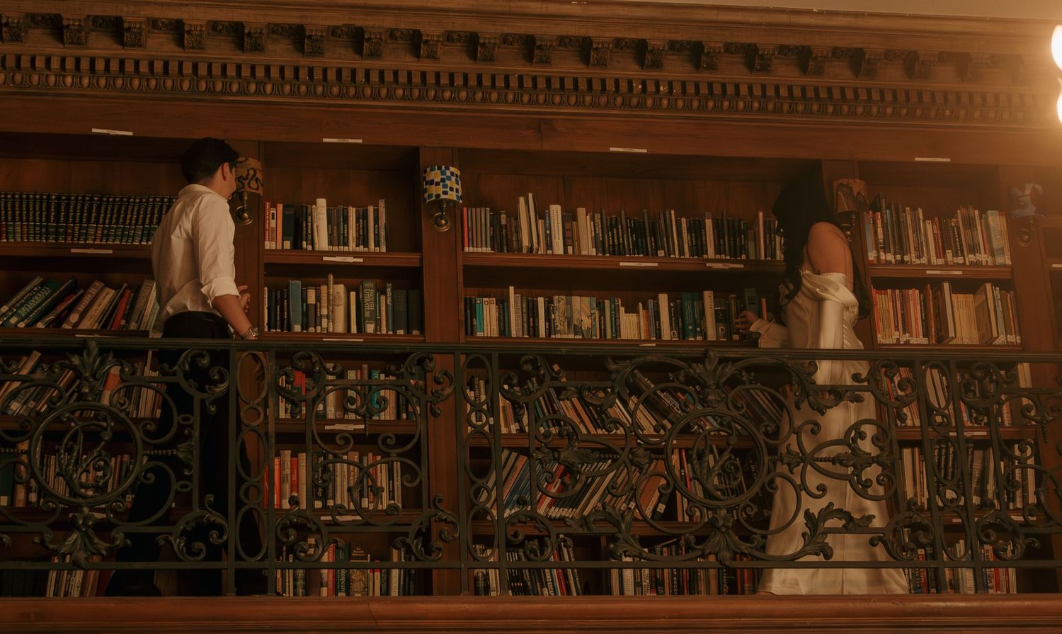 A warm-lit library interior with wooden bookshelves stretching along the walls in a vintage setting.