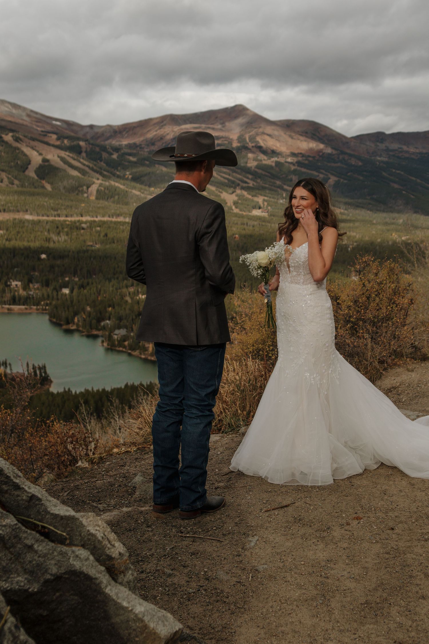 A couple shares a private moment on a mountain overlook with a scenic lake view.
