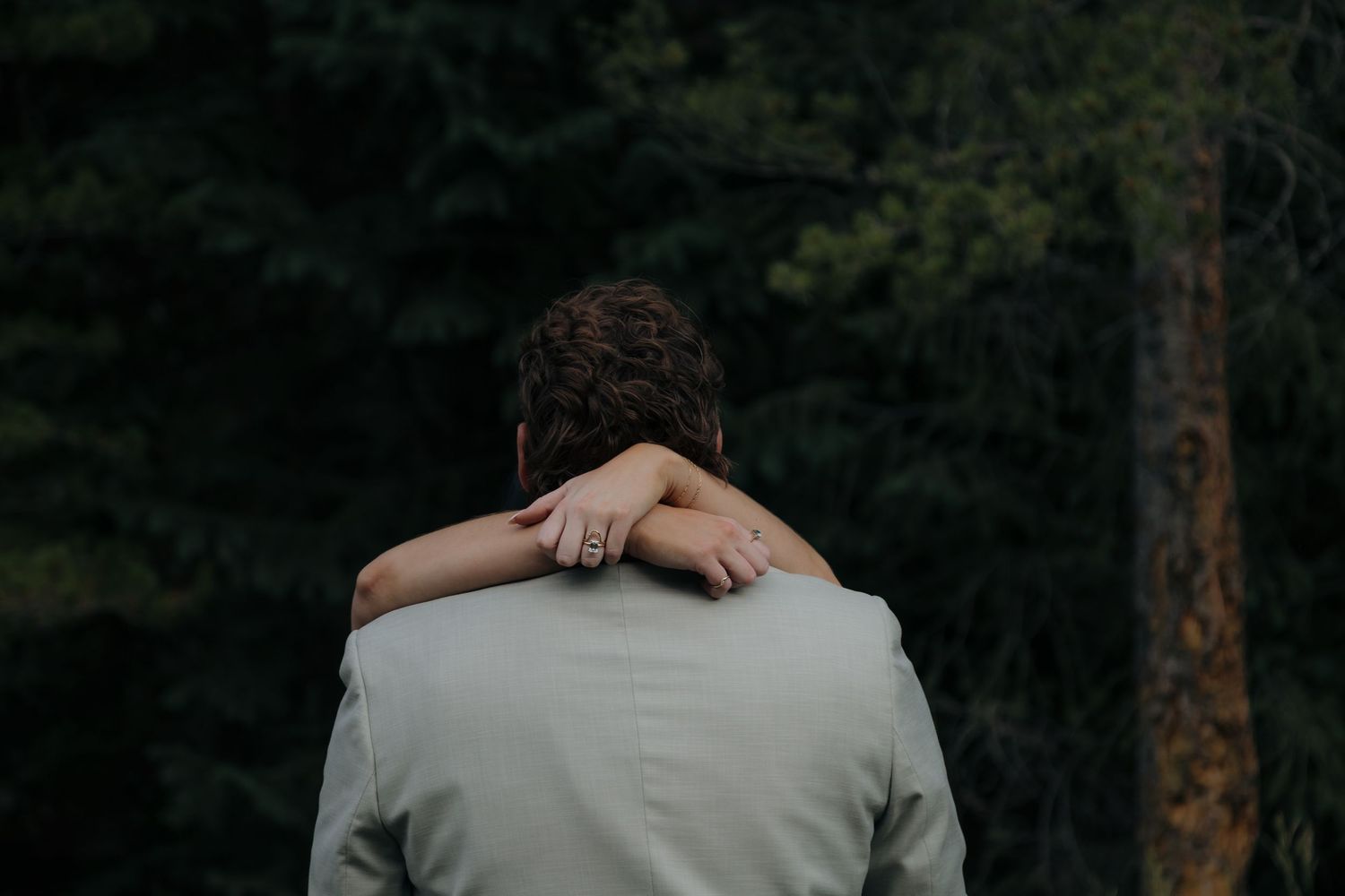 Close-up of brides arm draped over grooms shoulder, showing engagement ring against his light gray suit jacket.
