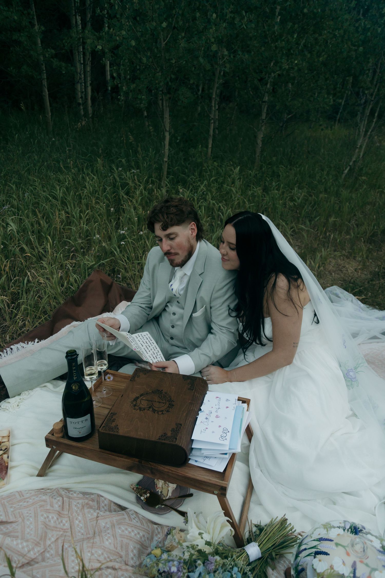 Bride and groom reading vow books together during intimate outdoor picnic elopement in forest.
