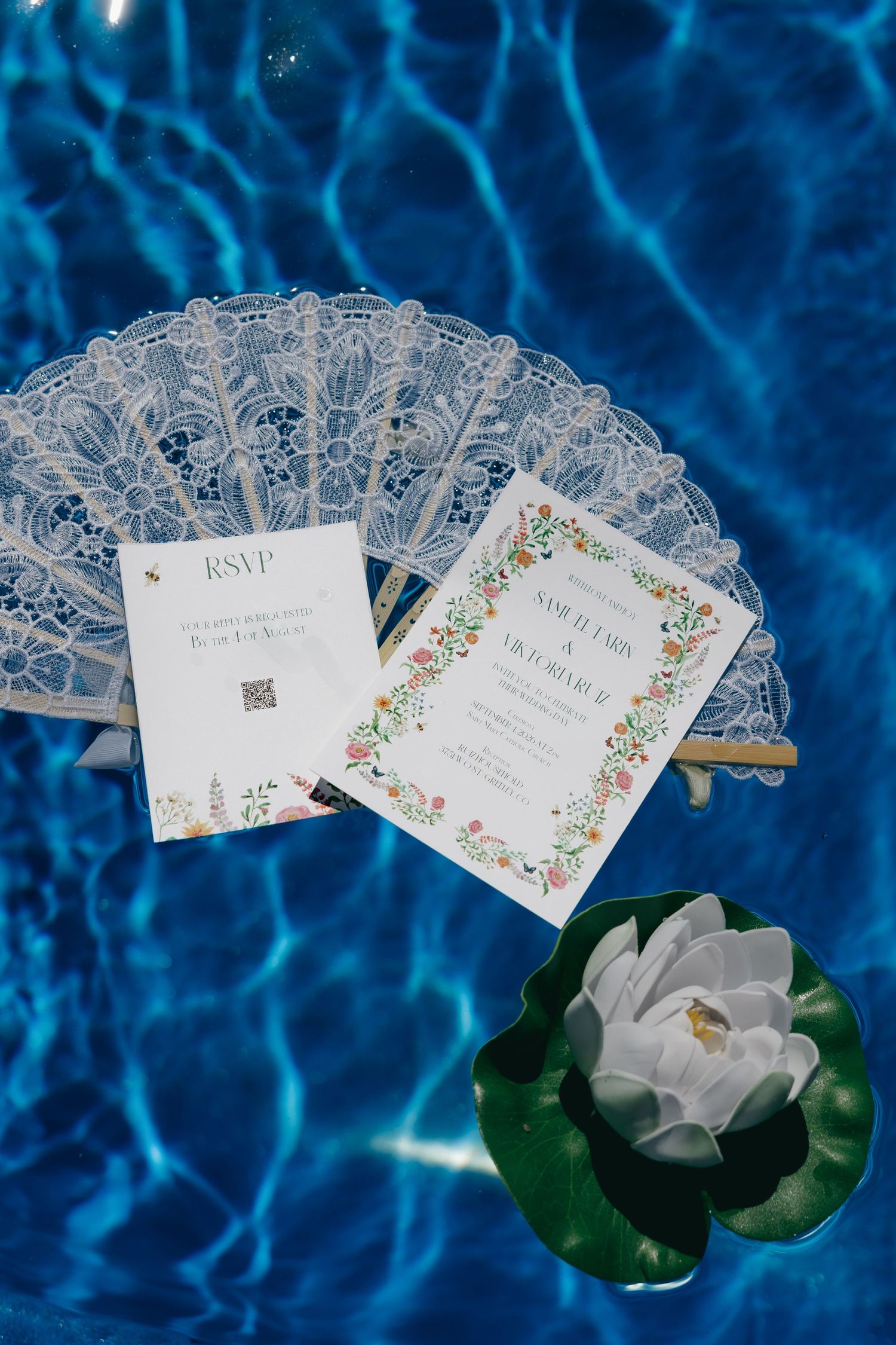 Elegant wedding invitation suite with lace fan and lotus flower floating on blue pool water.