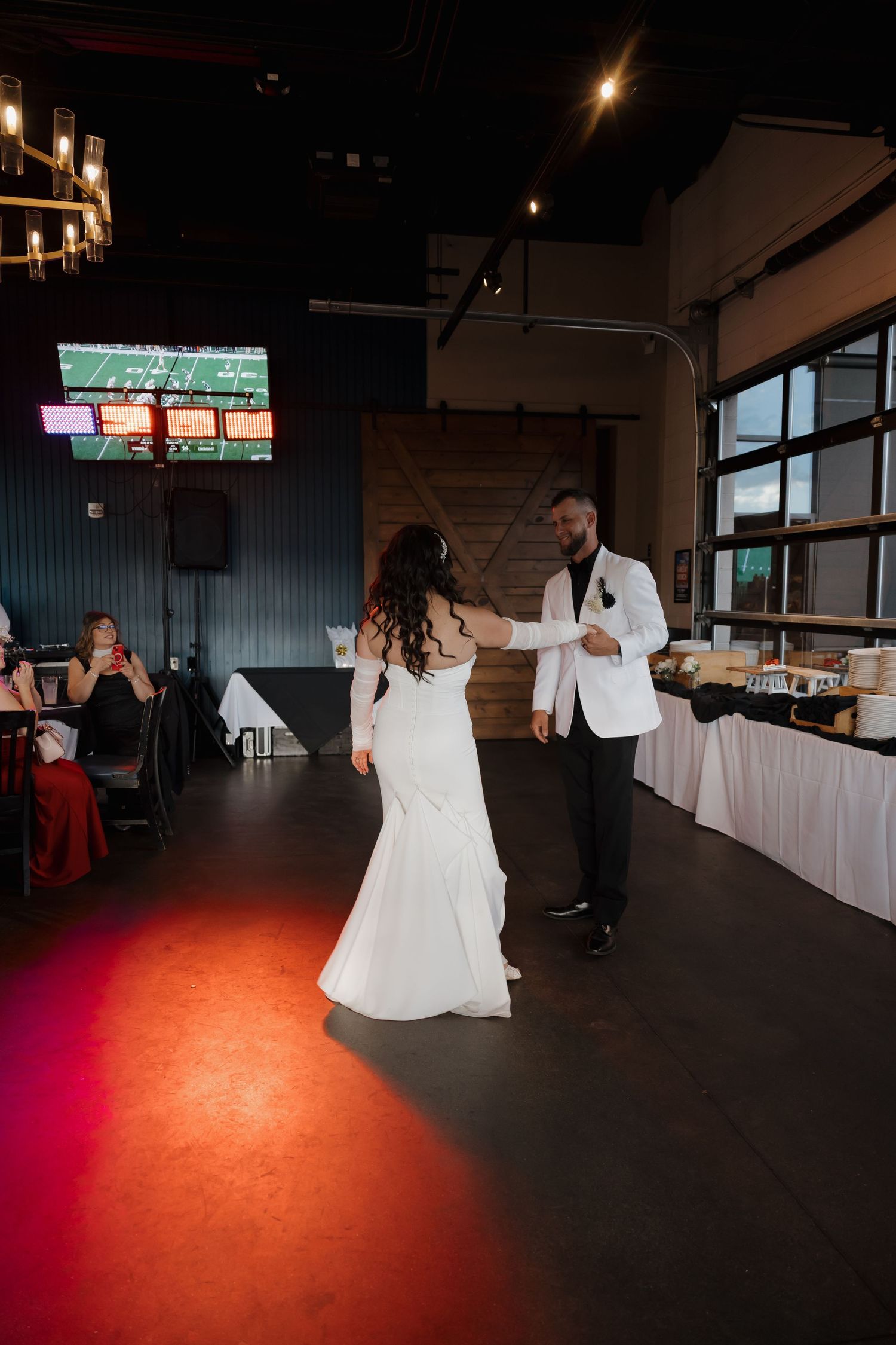 Bride and groom sharing first dance in modern wedding venue with barn wood backdrop.
