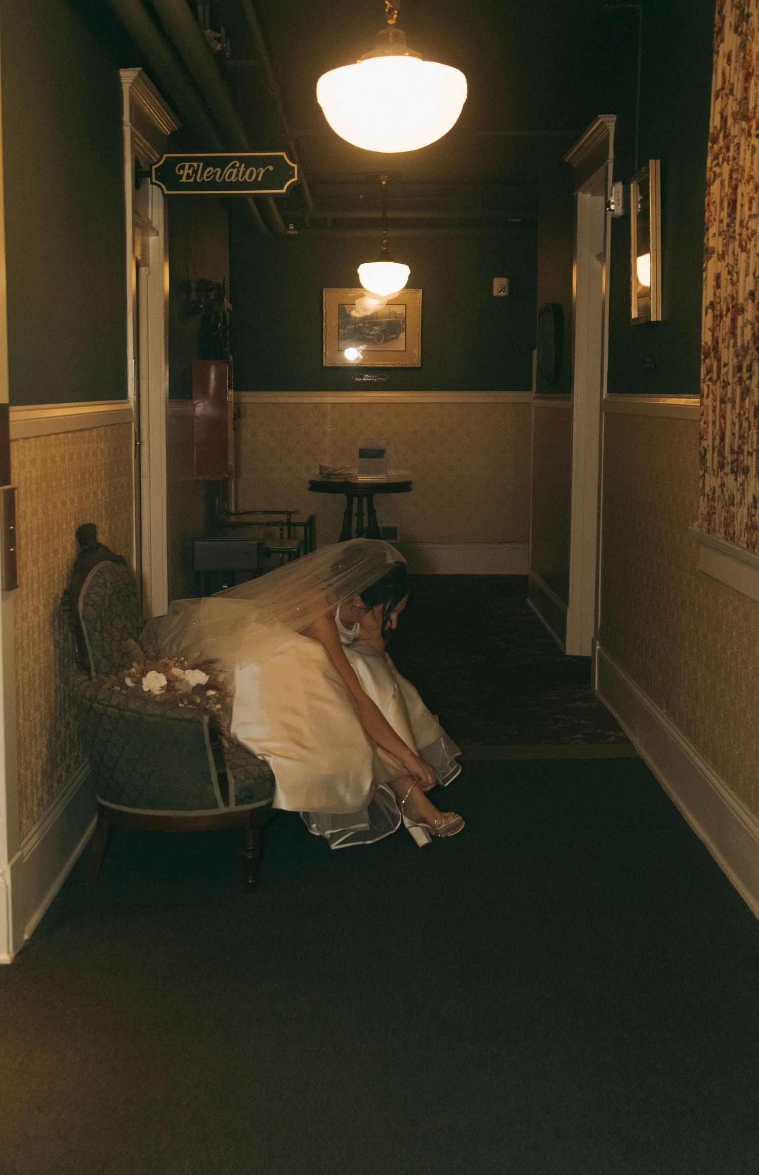 A dimly lit vintage hotel hallway with glowing pendant lights and floral wallpaper creates an eerie atmosphere.