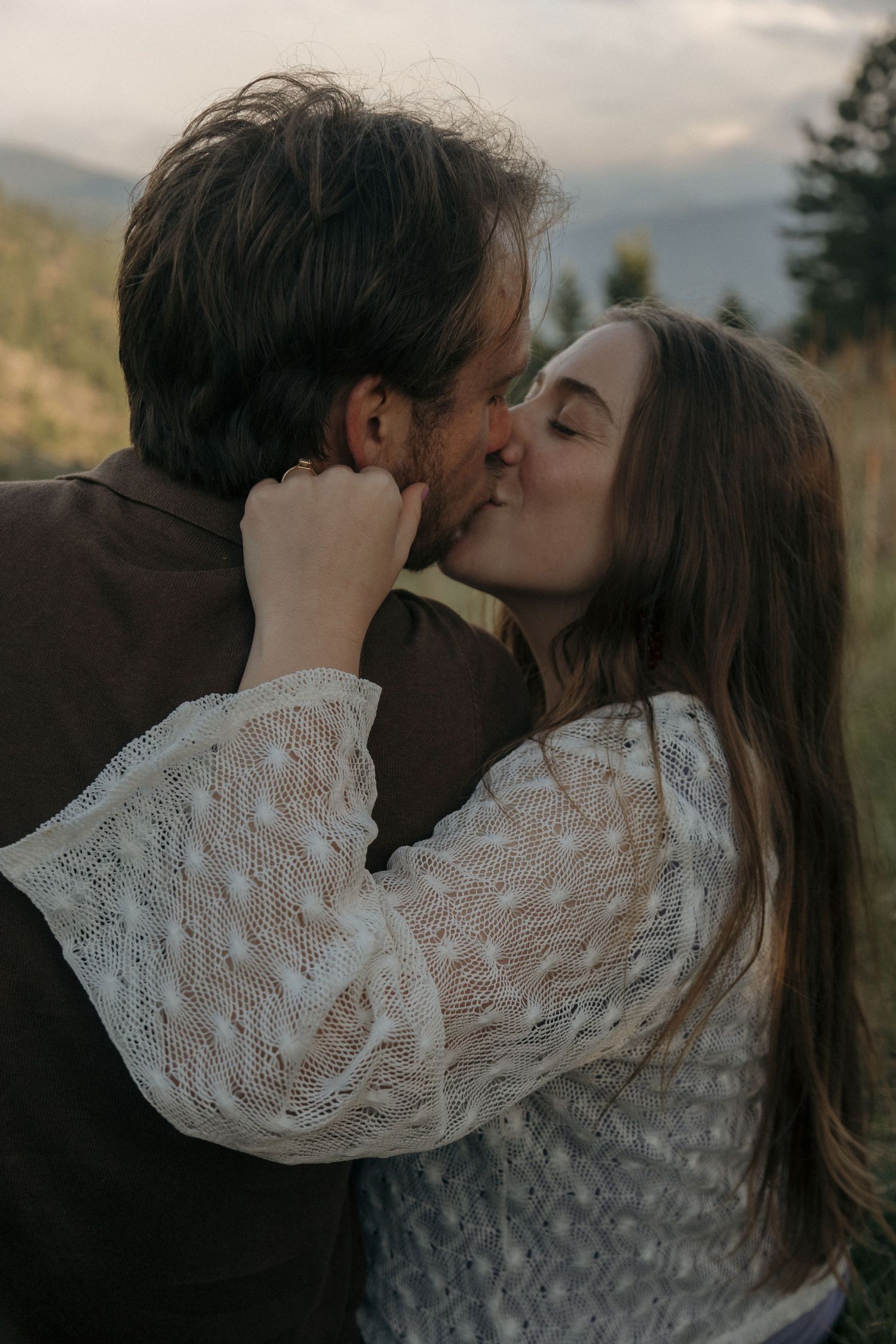 Couple sharing a tender kiss outdoors with misty mountain landscape in background.