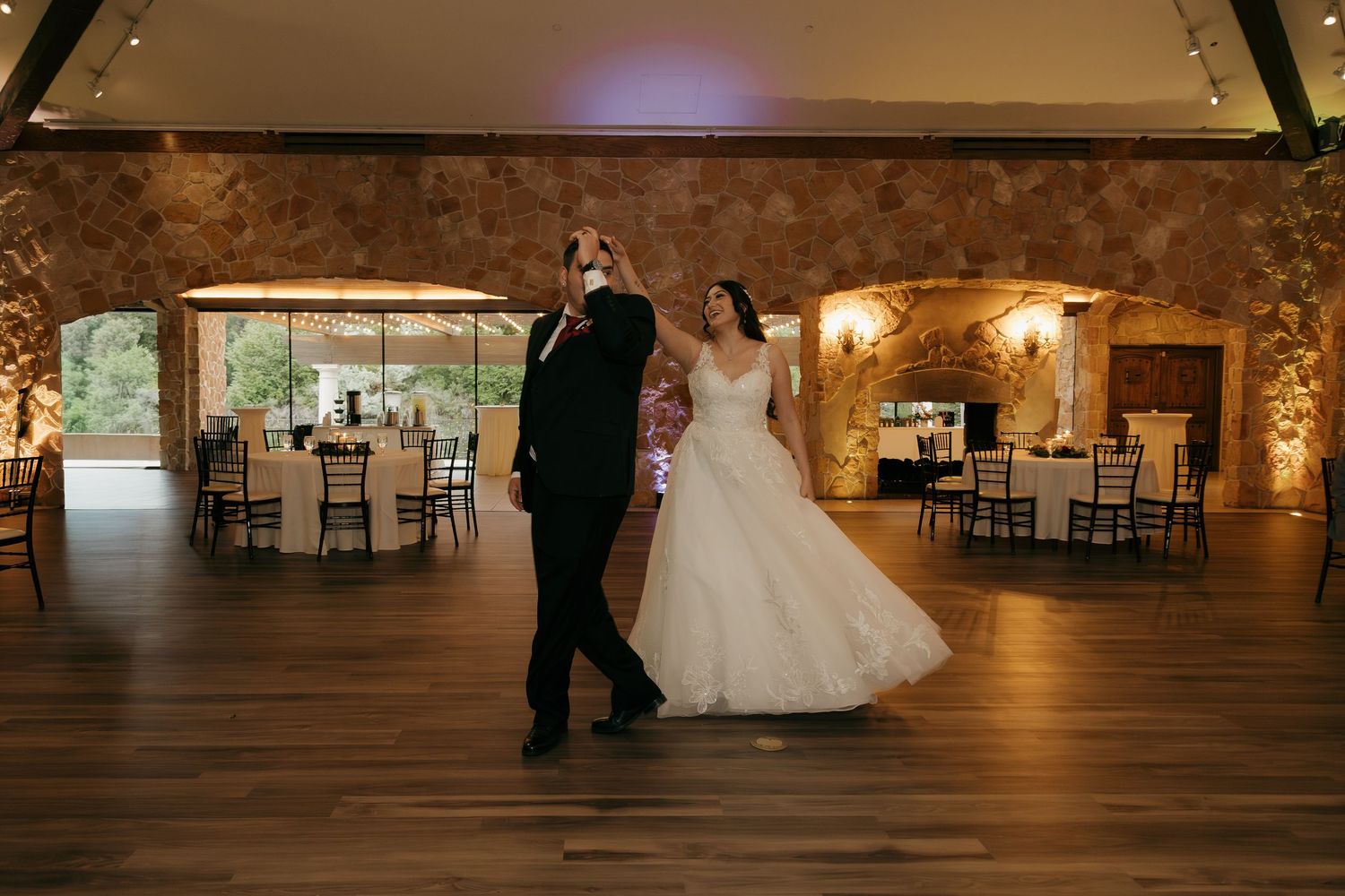 Bride and groom sharing first dance in elegant rustic stone wedding reception hall.