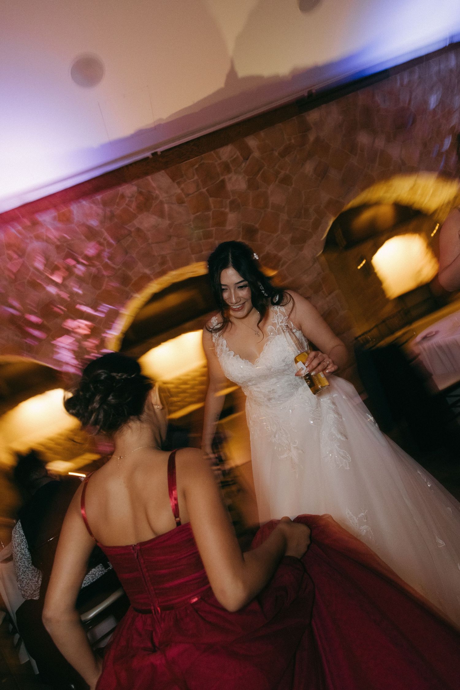 Bride dances joyfully with a guest in a red dress on the wedding reception dance floor.