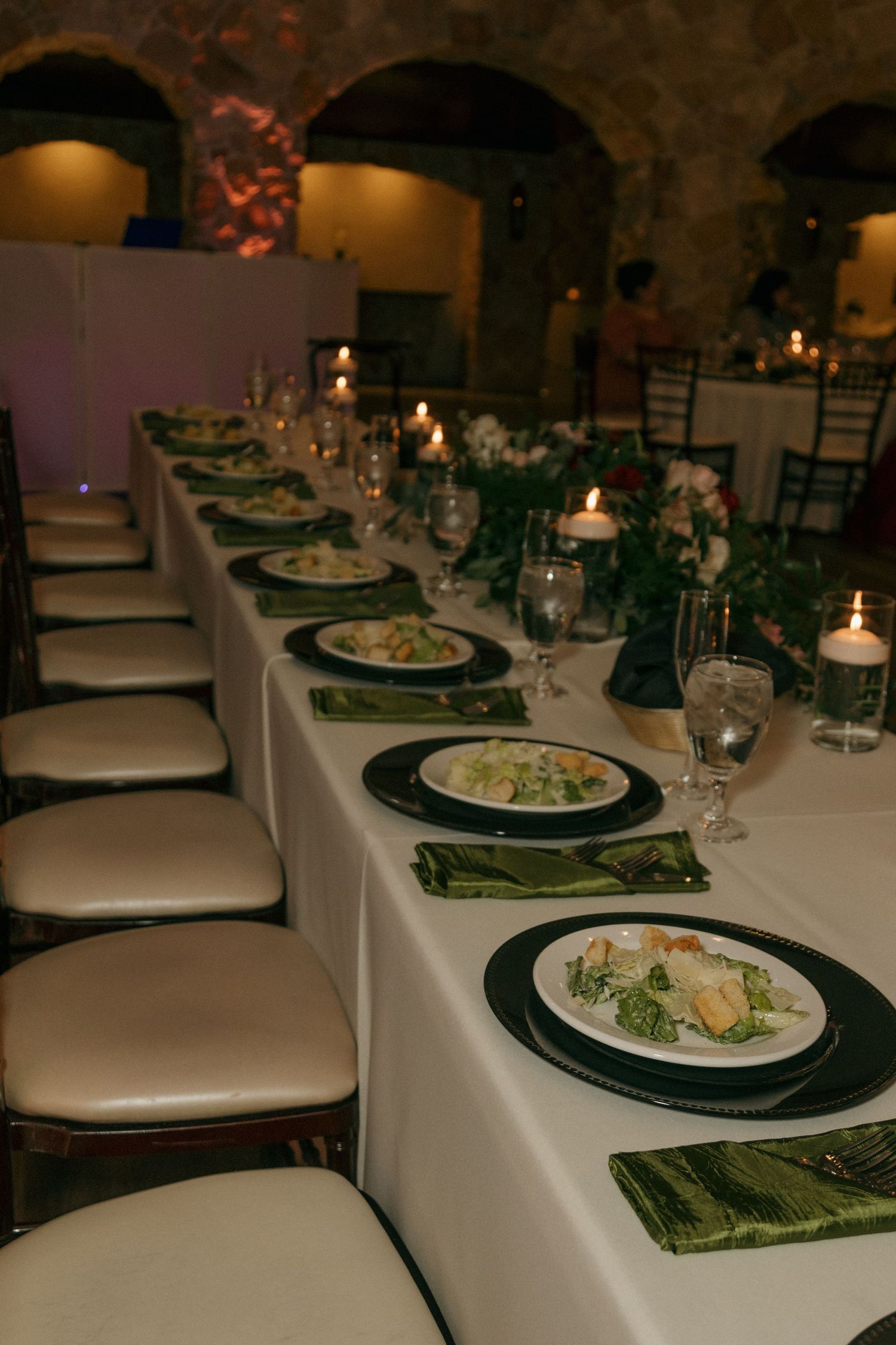 Elegant wedding reception dinner table set with green chargers, salad plates, candles, and floral centerpieces.