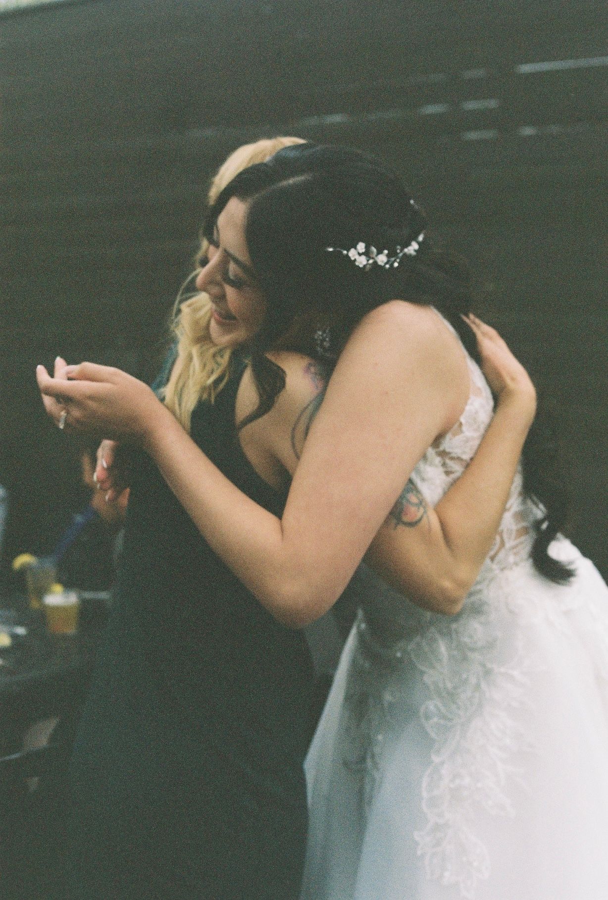 Bride in lace gown shares an emotional hug with a blonde guest during wedding reception celebration.