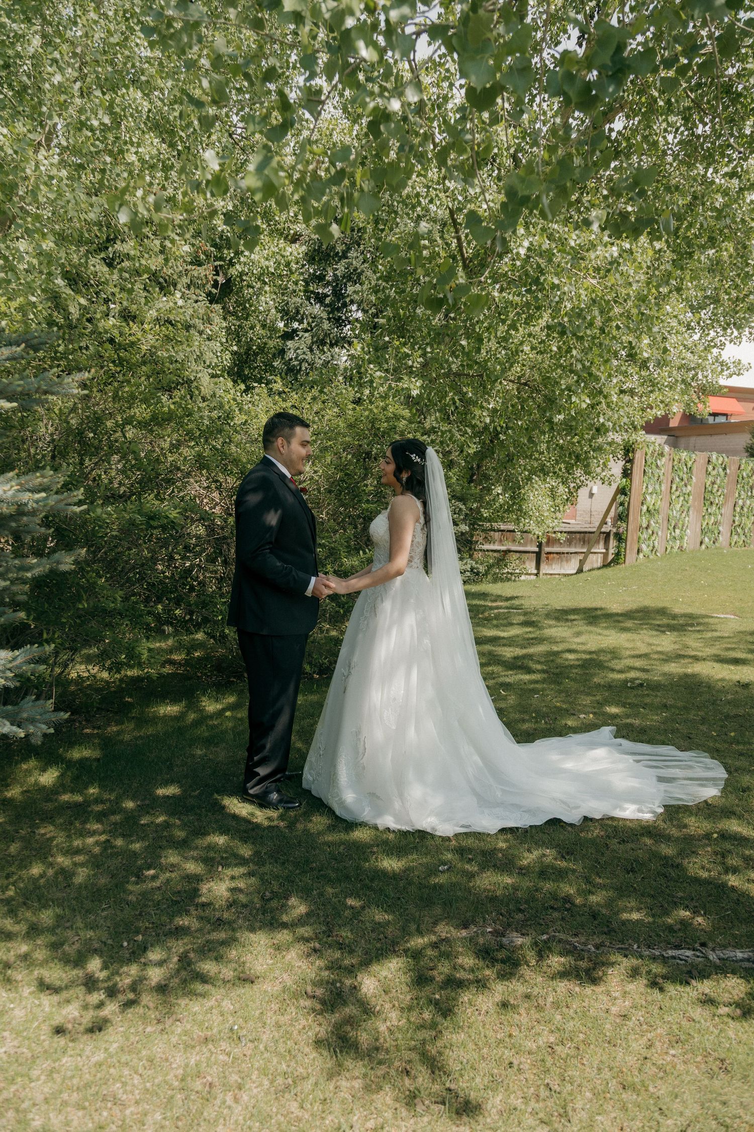 Bride and groom holding hands outdoors under lush green trees on their wedding day.