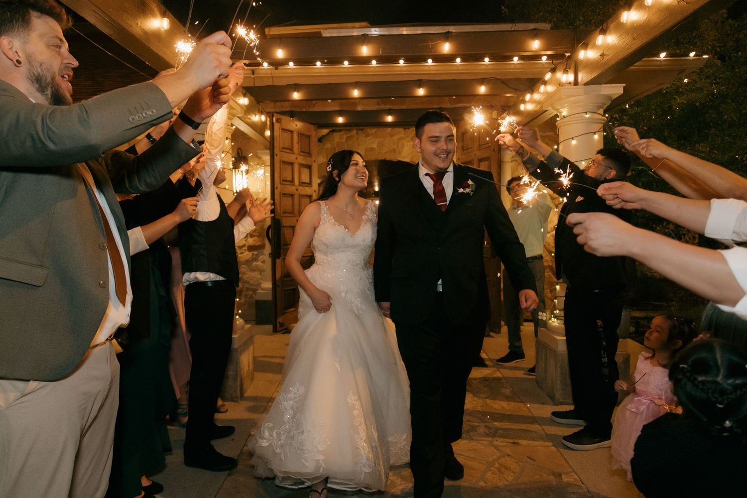 Bride and groom exit through a sparkler tunnel during their wedding grand exit at night.