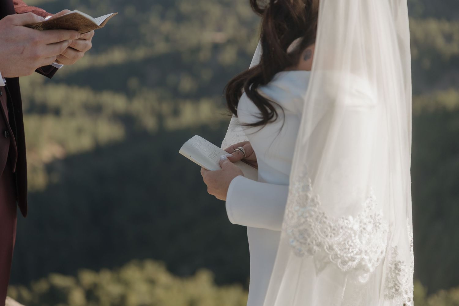Bride in lace-trimmed veil reads heartfelt wedding vows during outdoor mountain ceremony.