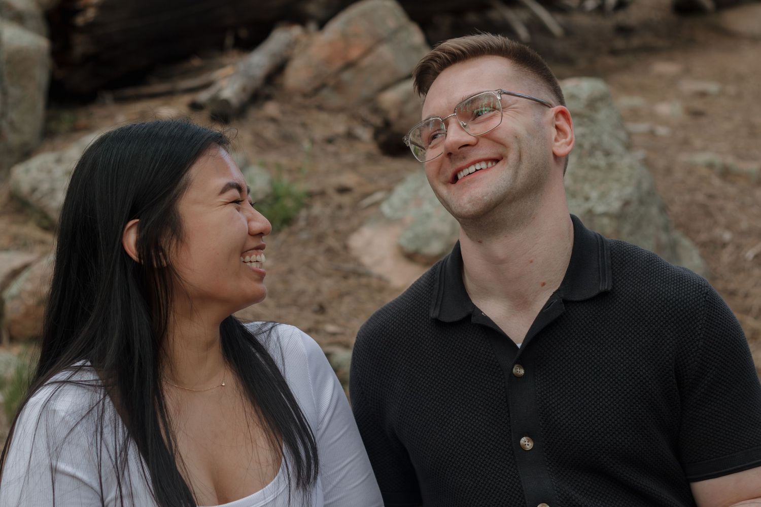 A couple shares a joyful moment while sitting on rocks outdoors.