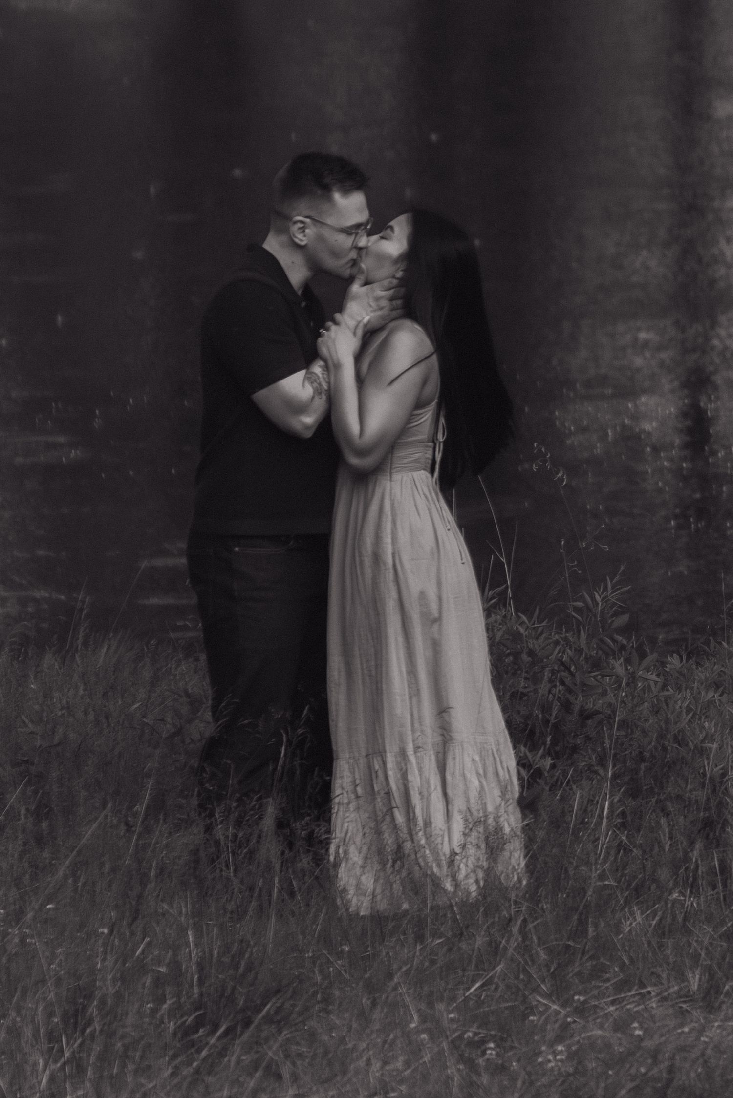 A black and white romantic portrait of a couple sharing an intimate moment against a dark background.