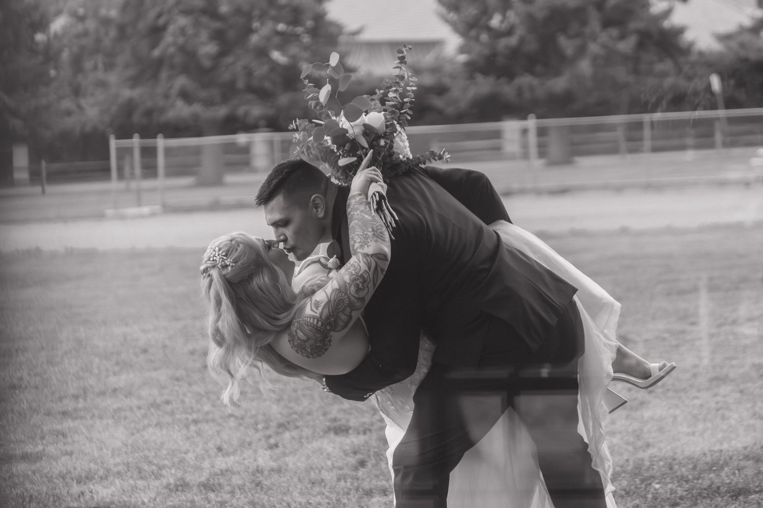 A black and white photo of a couple sharing a playful dip pose in a field.