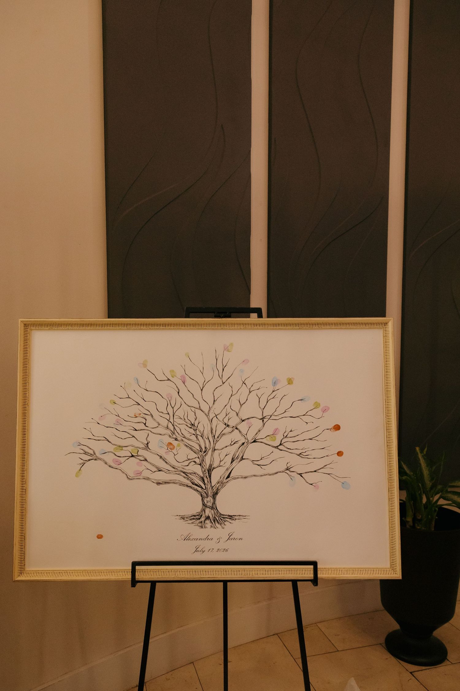 Fingerprint guest book tree artwork displayed on easel at wedding reception venue.