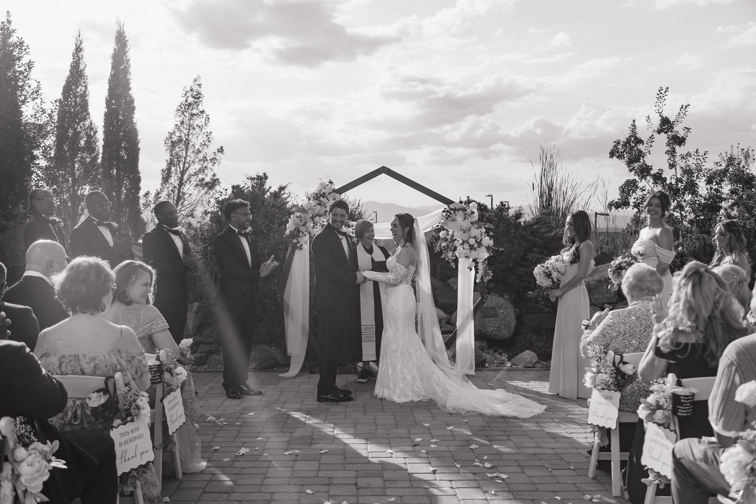 Black and white photo of outdoor wedding ceremony with guests seated along aisle.