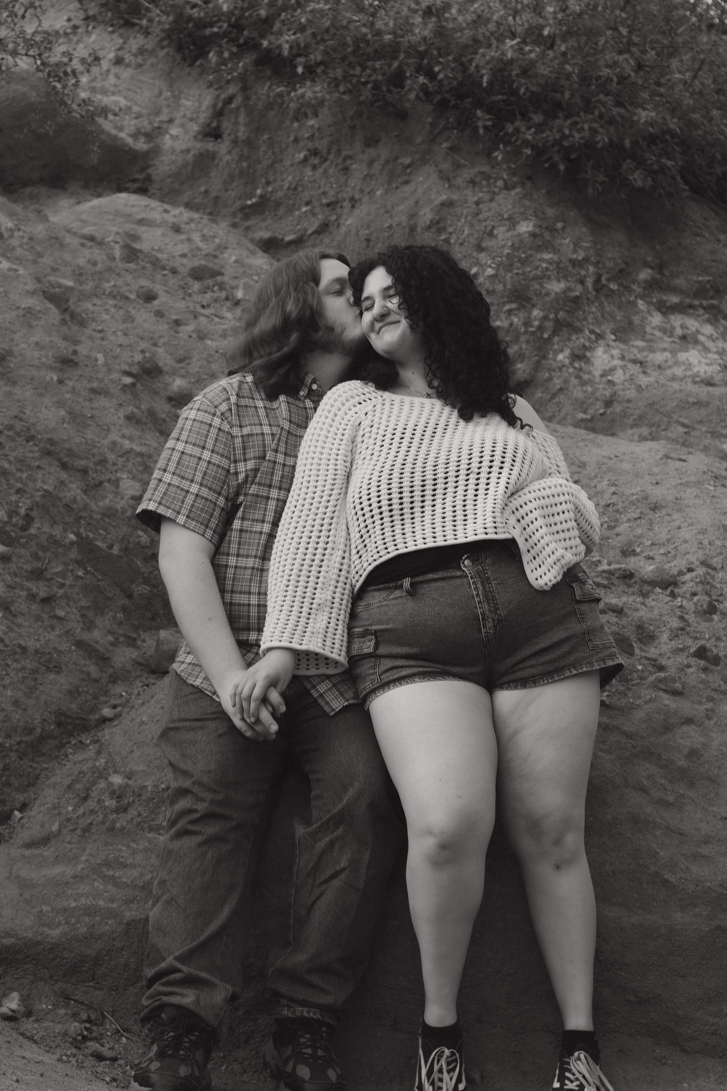 A romantic black and white portrait of a couple embracing against a rocky backdrop.