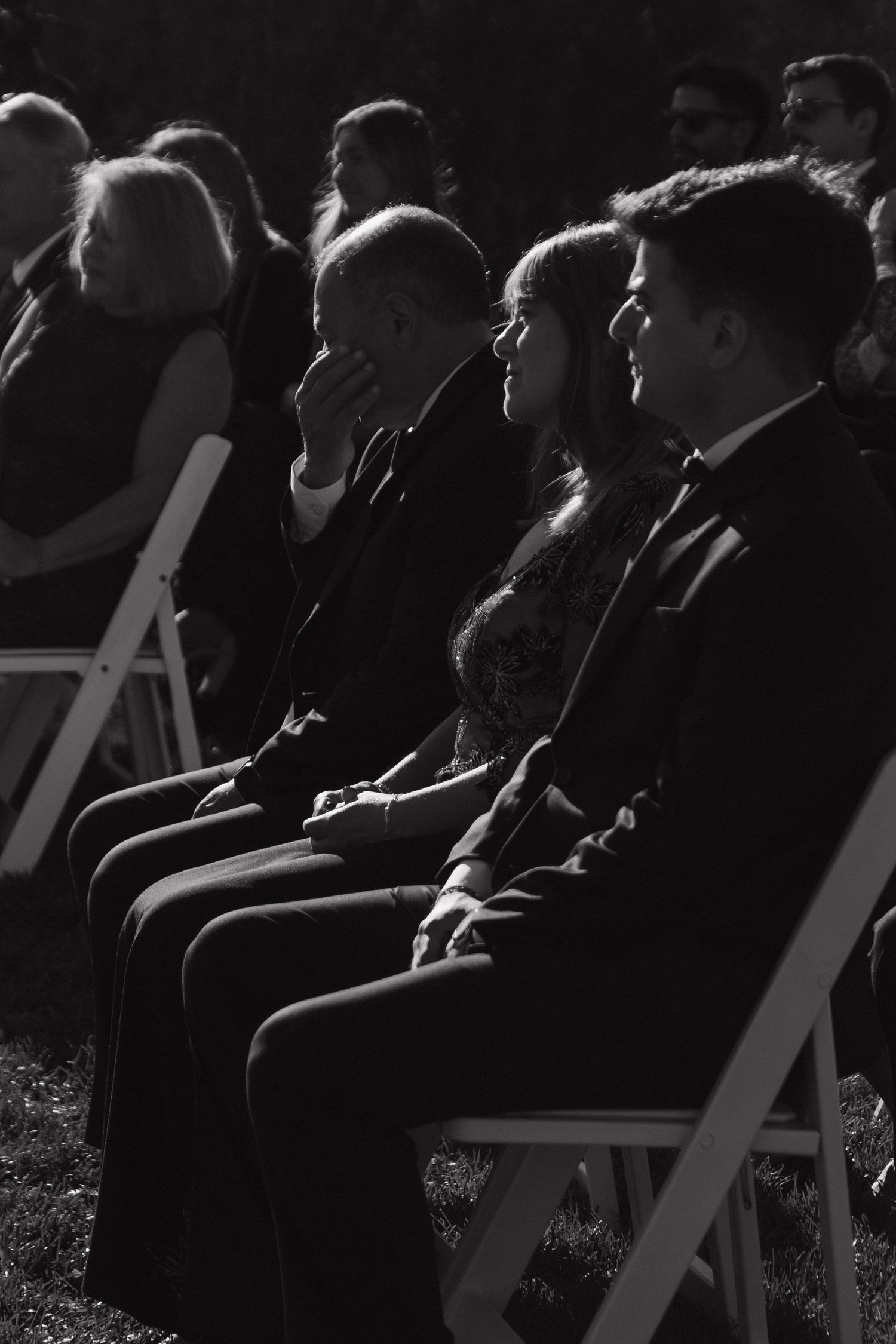 Wedding ceremony guests seated in white chairs during outdoor service.