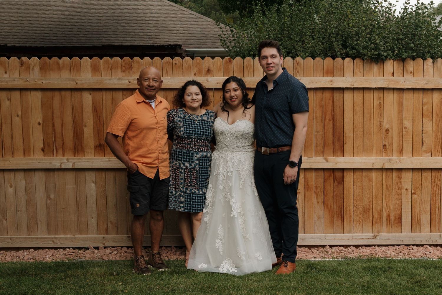 People pose together for photos at an outdoor event in front of a wooden fence.