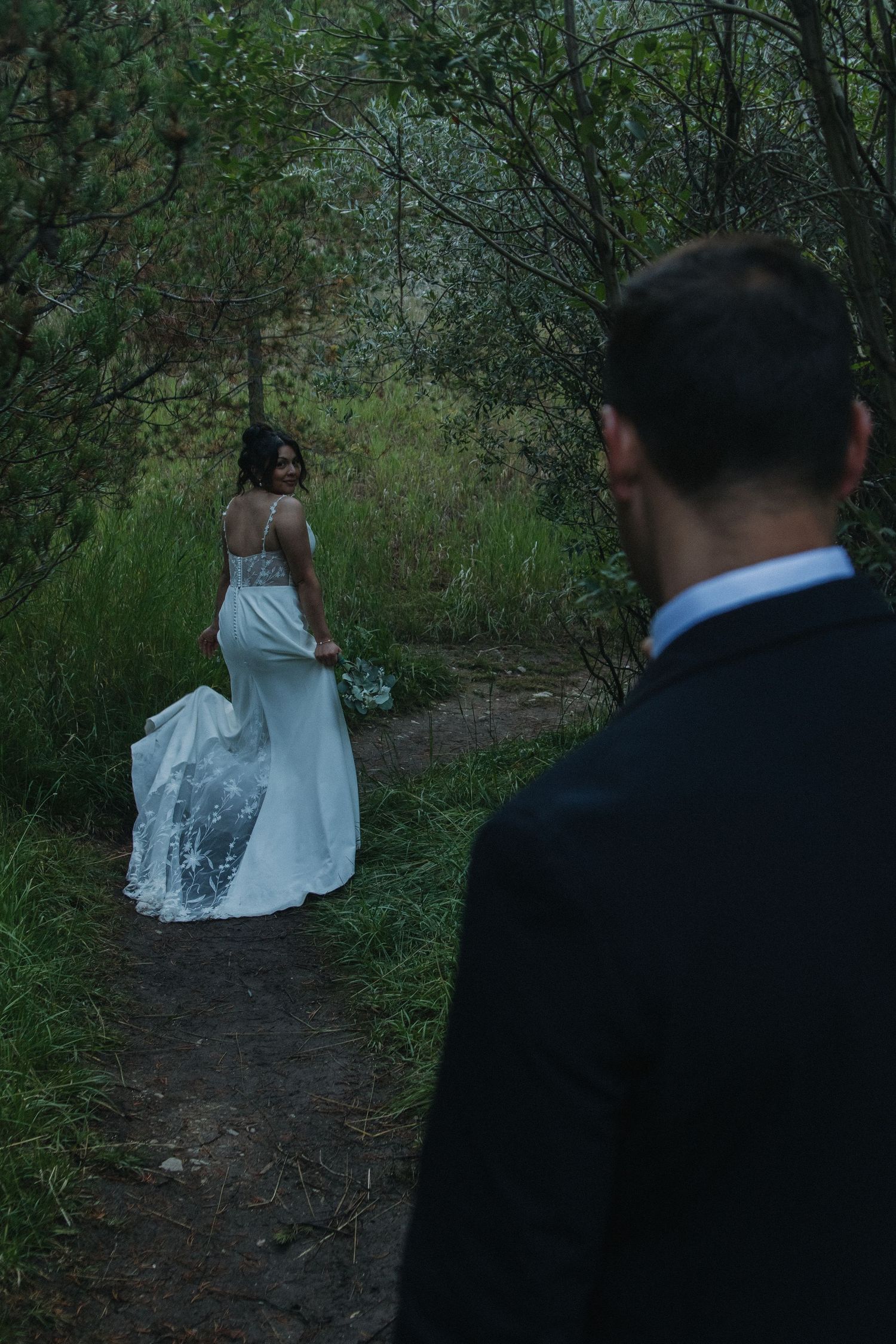 Wedding couple walking through lush green mountain trail during sunset.