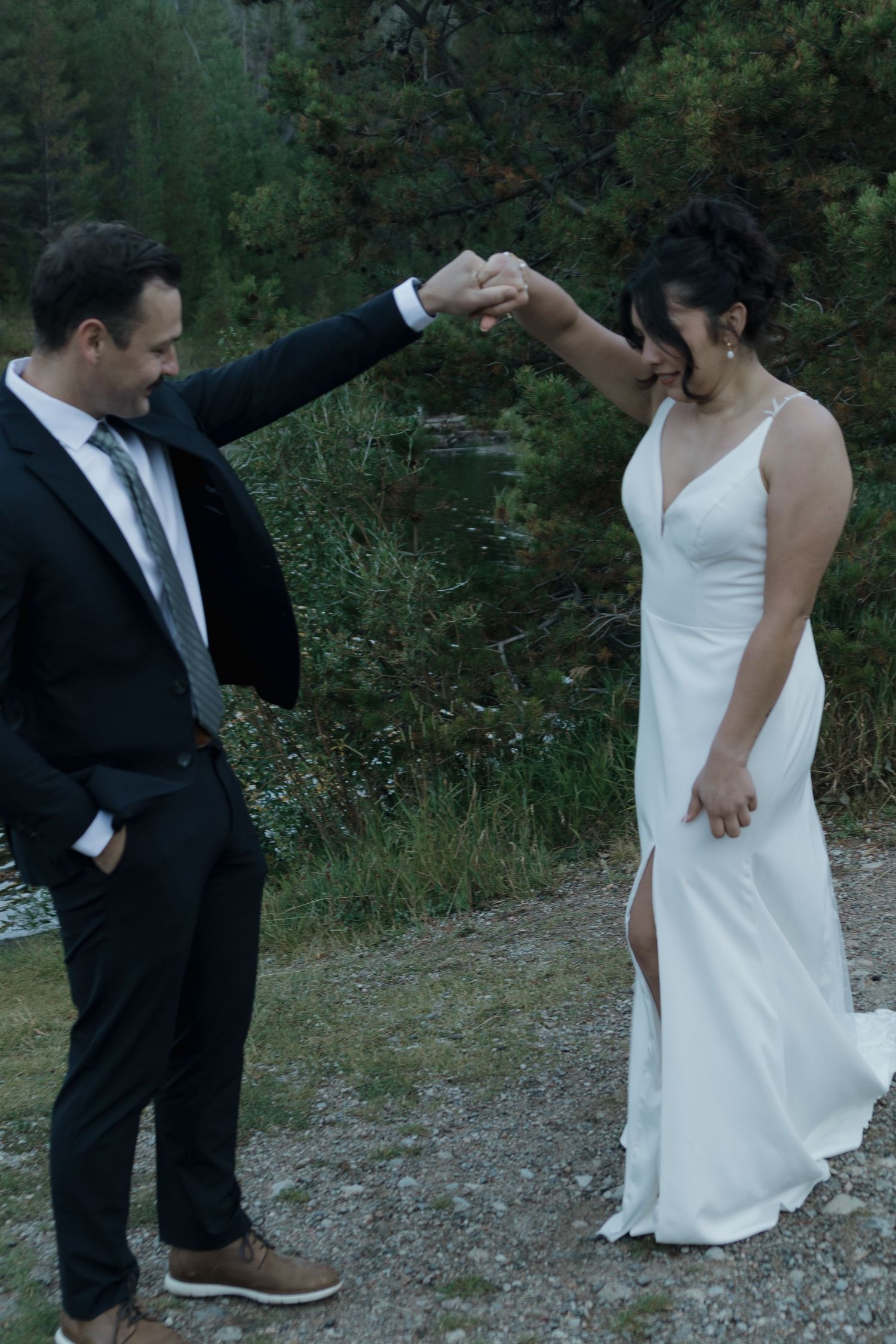 A couple in wedding attire dancing together on a mountain path surrounded by lush greenery.
