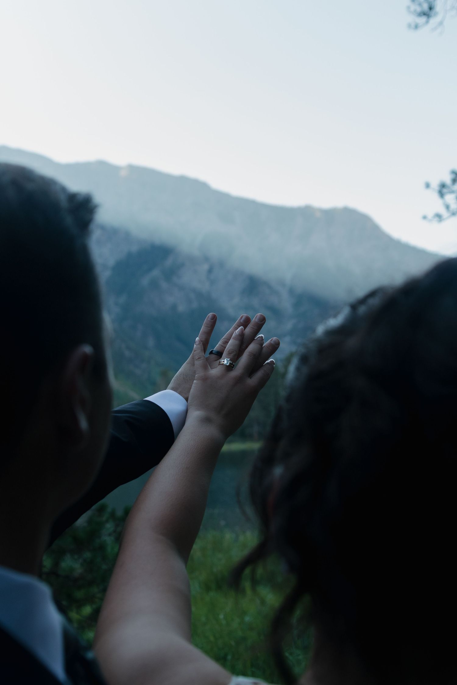 Raised hands displaying a wedding ring with majestic mountains in the background.