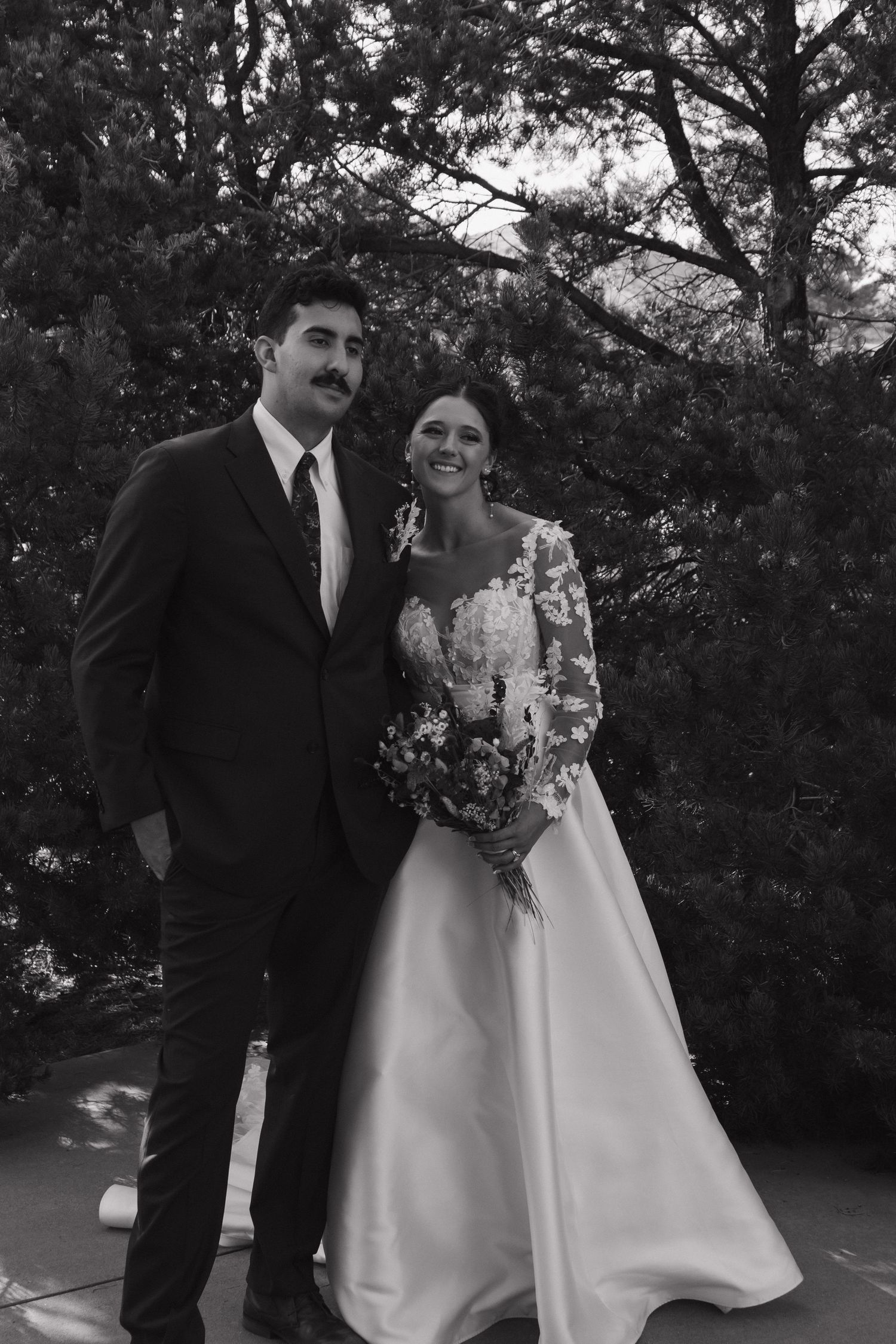 Black and white portrait of wedding couple outdoors with trees in background.