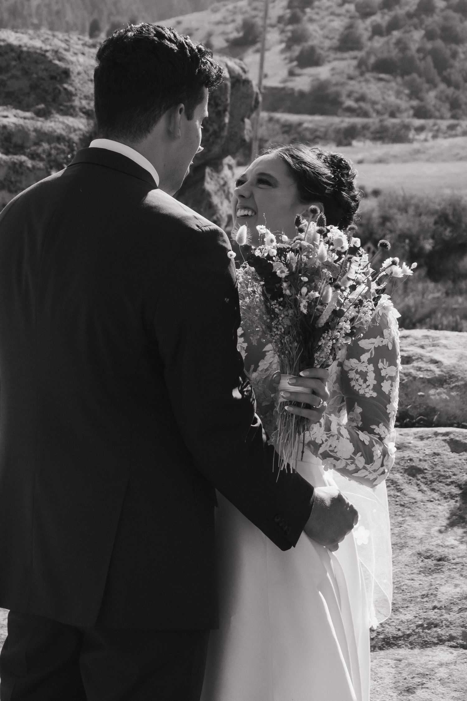 Romantic wedding couple shares intimate moments against a mountainous backdrop holding a delicate floral bouquet.