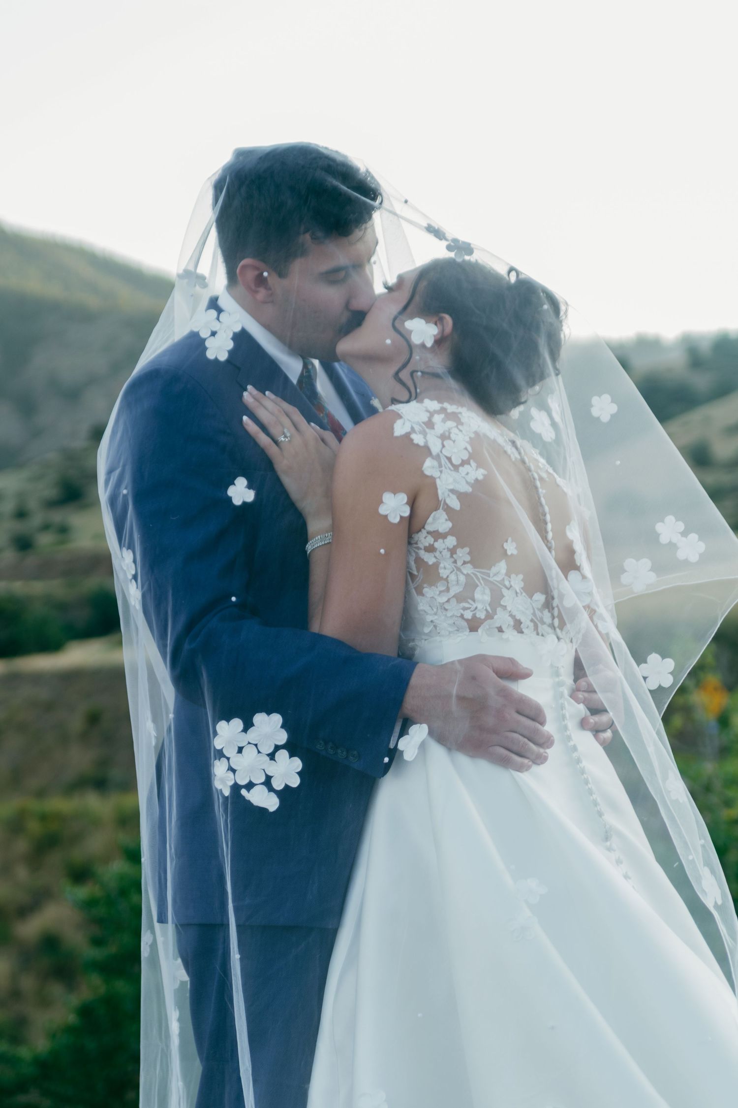 Romantic outdoor wedding moment with flowing veil against mountain backdrop.