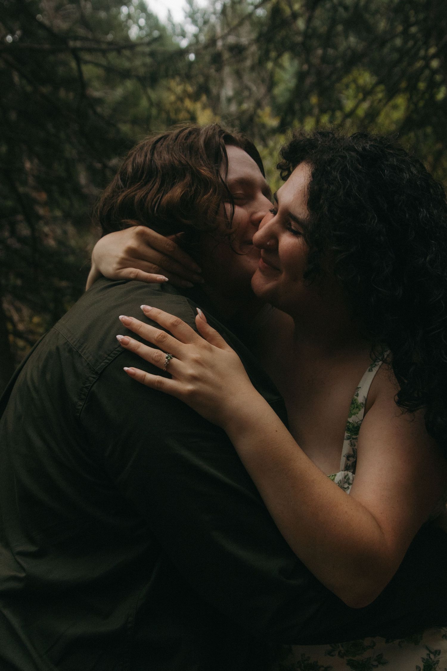 Intimate romantic moment captured in shadowy natural outdoor setting with soft backlighting.