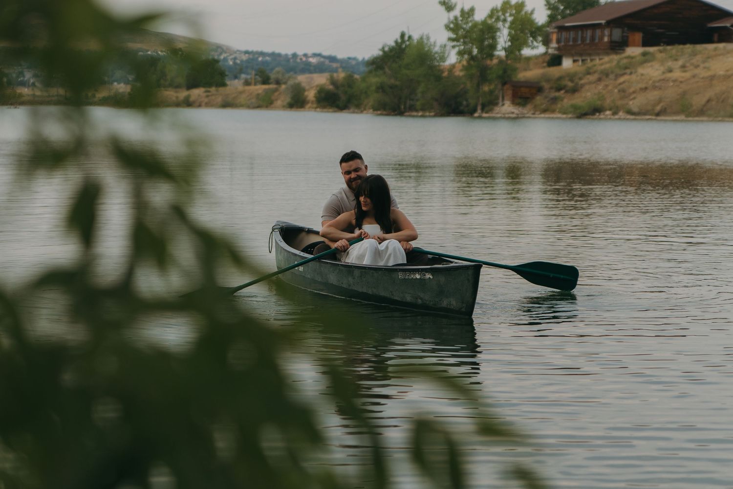 Someone paddling a canoe on a calm lake near a hillside home during a peaceful afternoon.