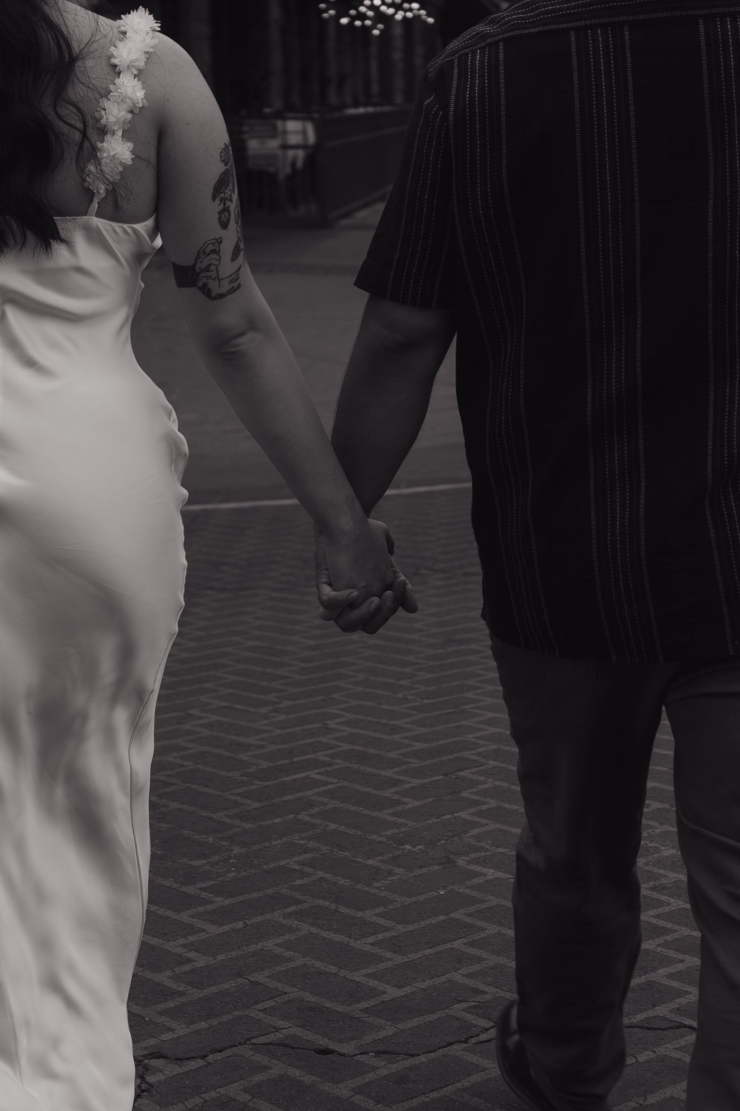 Black and white image of a couple holding hands while walking on a brick pathway.