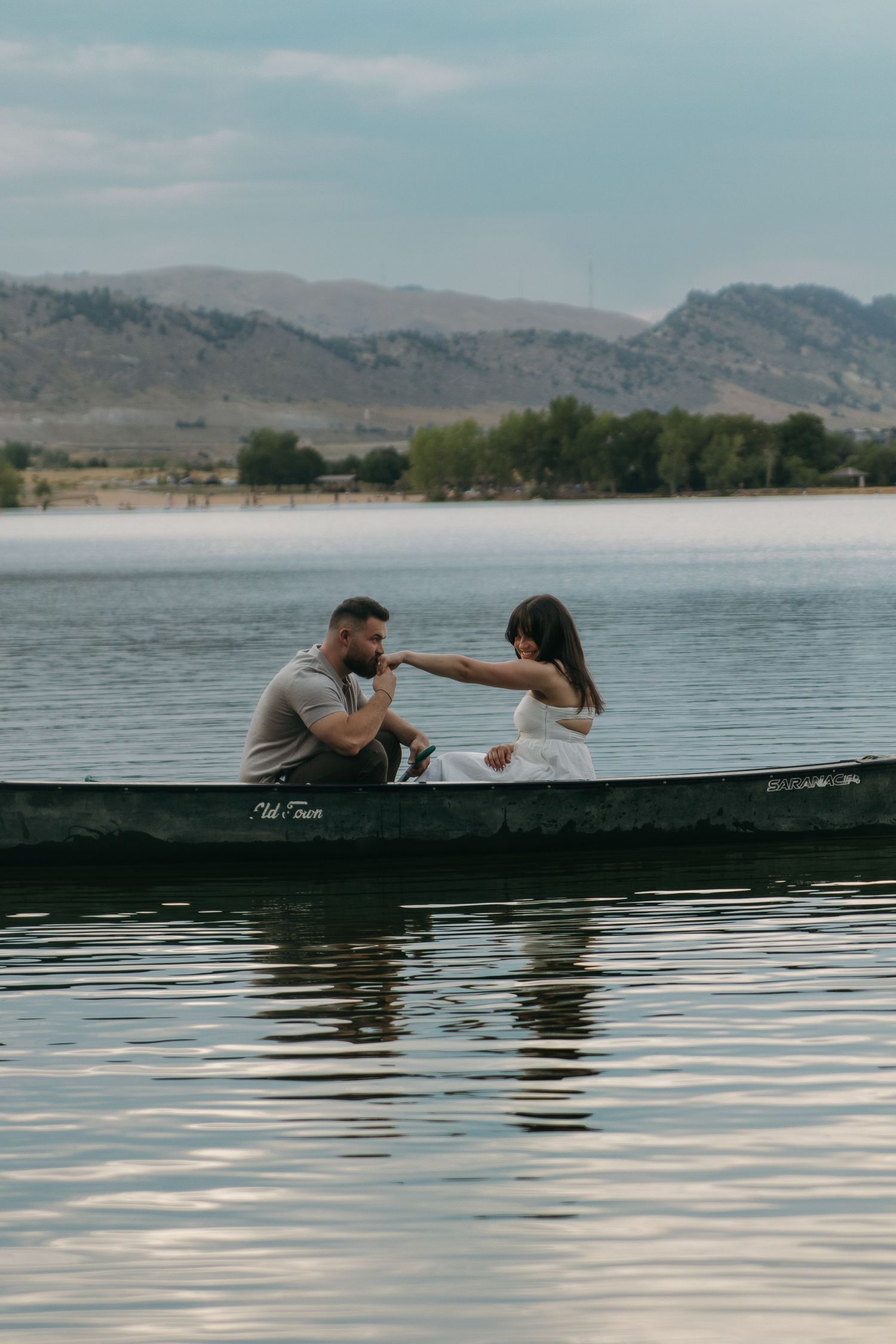 A canoe floats on a serene lake with mountains and blue sky in the background.