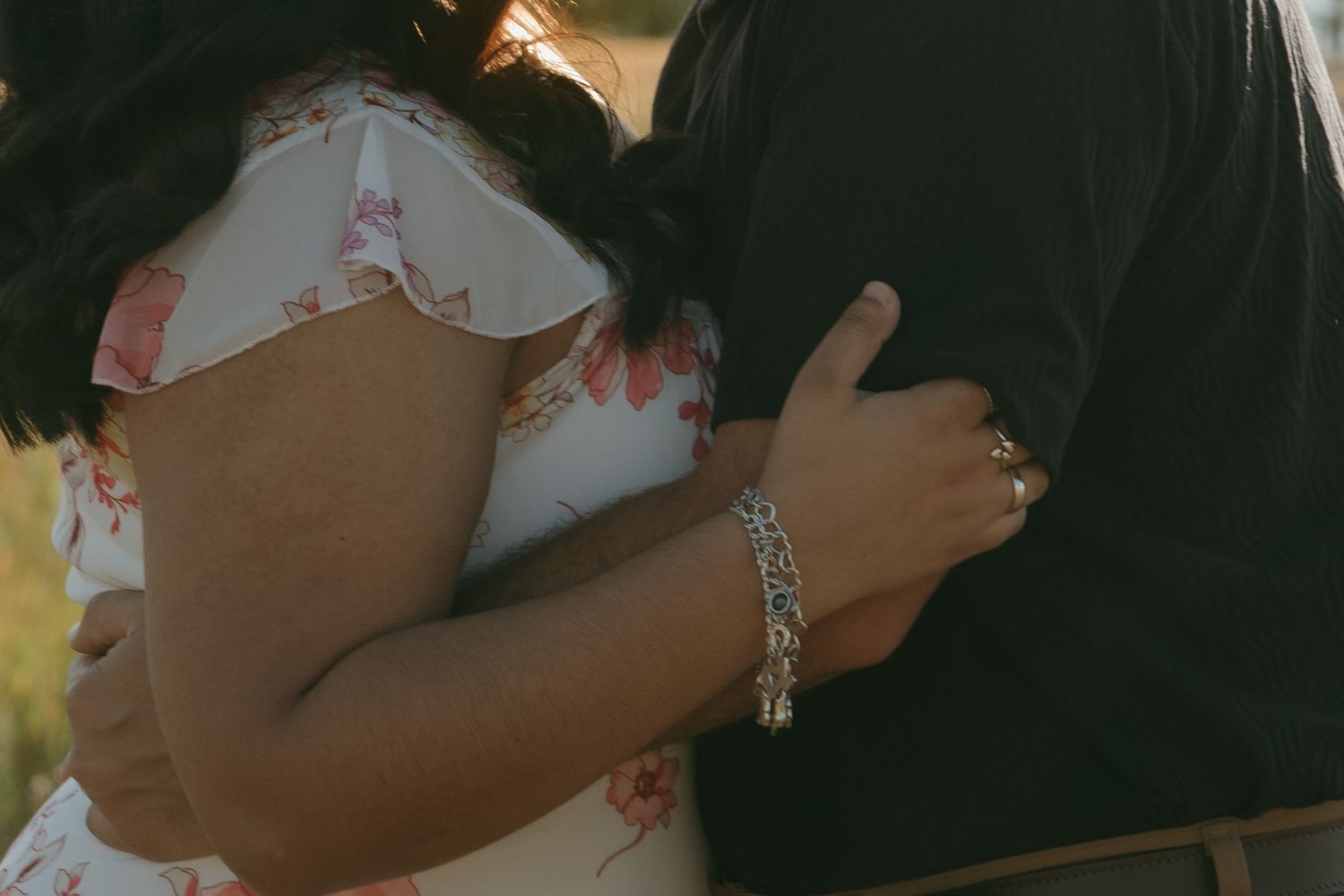 Close-up detail of hands embracing while wearing floral dress and dark clothing.