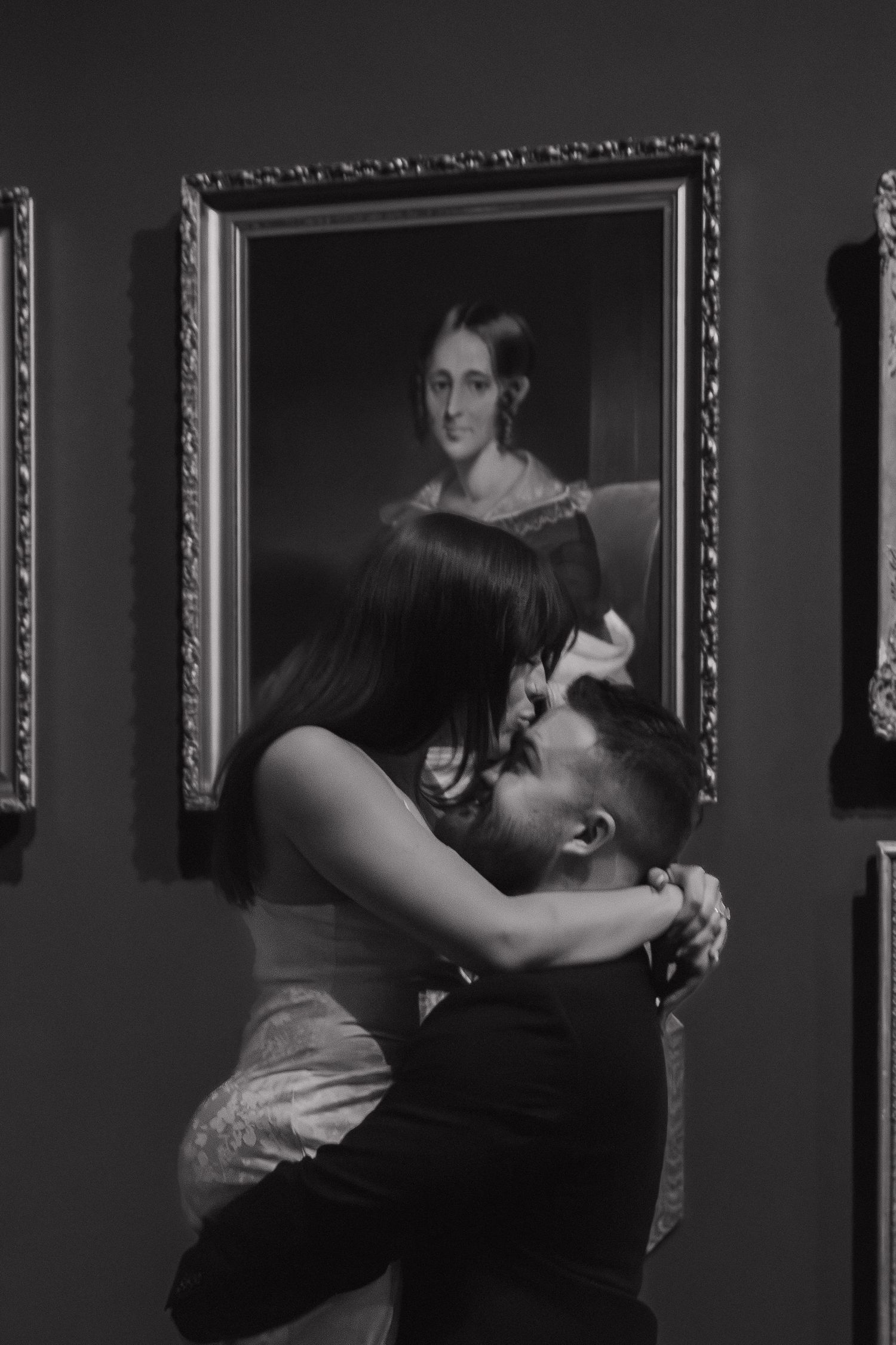Dimly lit gallery space showing figures moving in front of framed portraits.