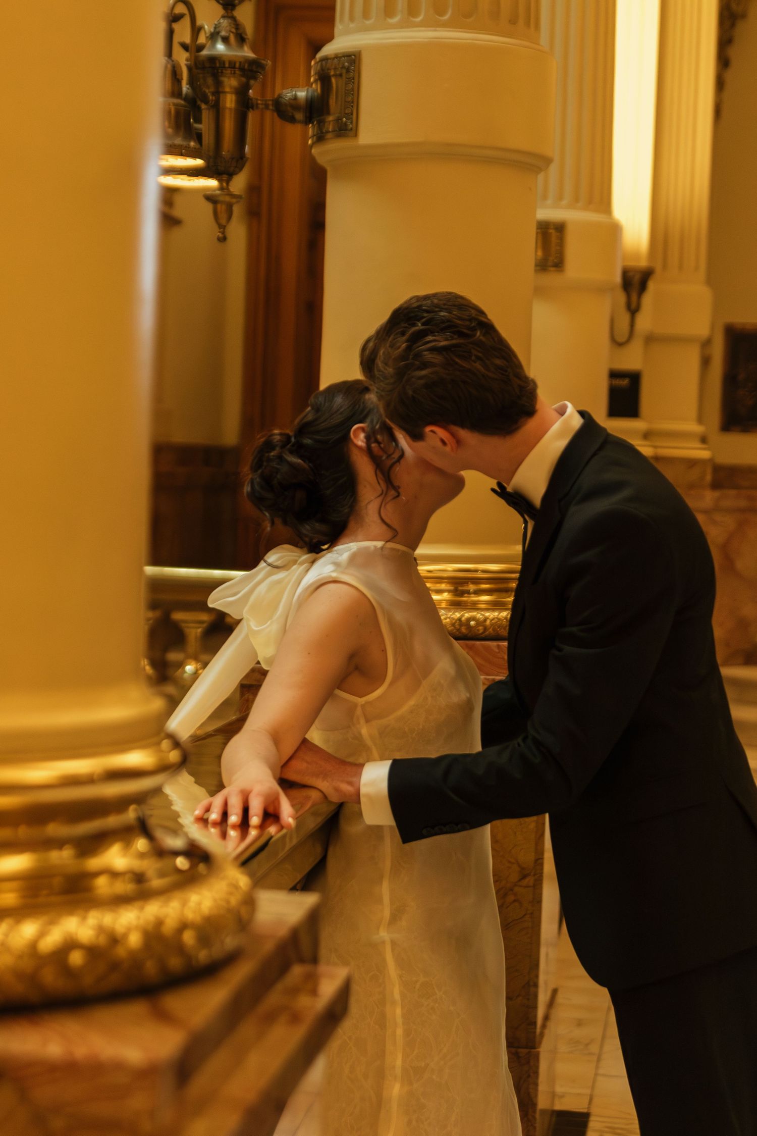 A couple dances together in an elegant room with golden lighting and ornate columns.
